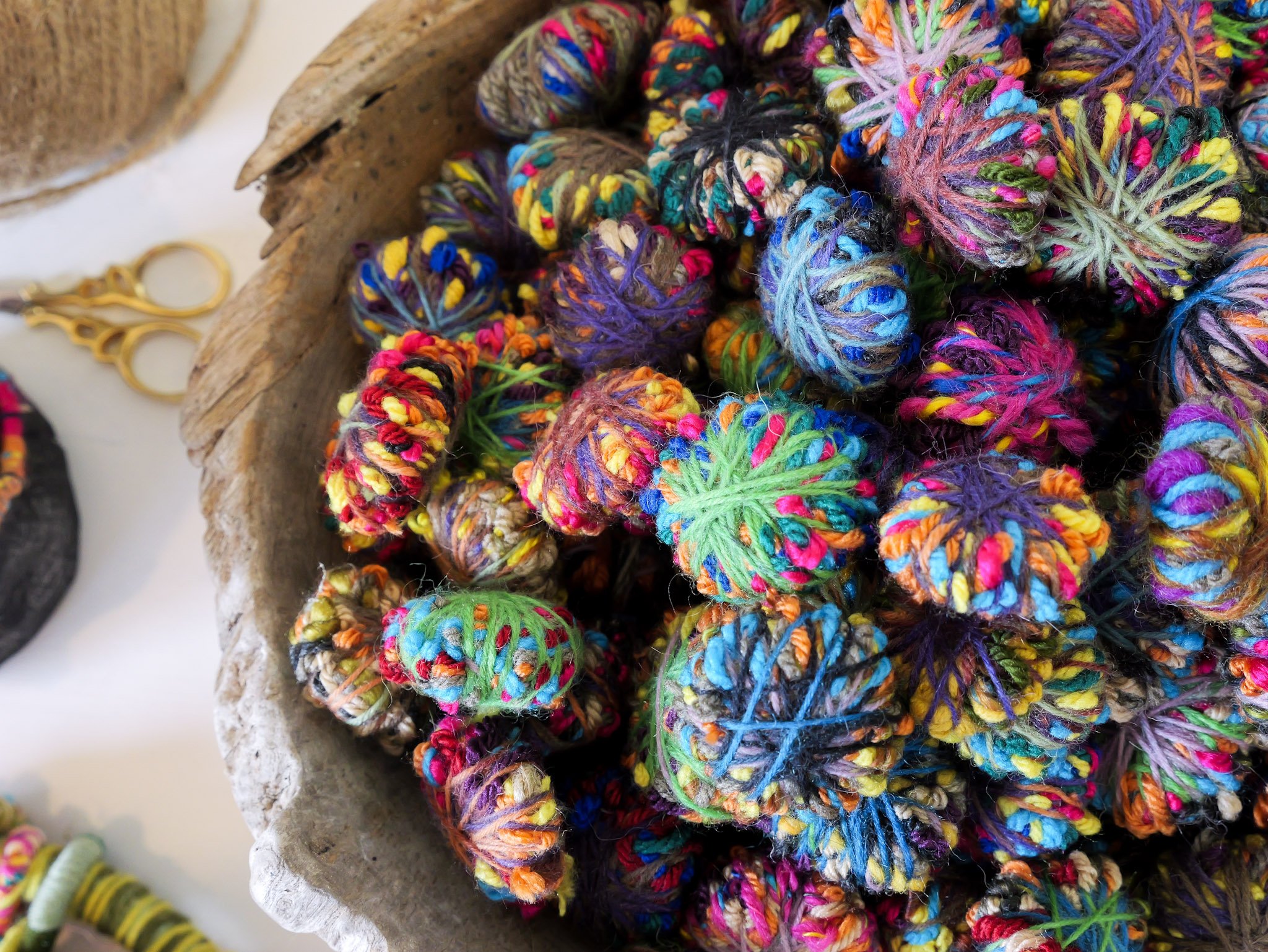 Colorful multicolored yarn balls in a wooden bowl with craft scissors nearby.