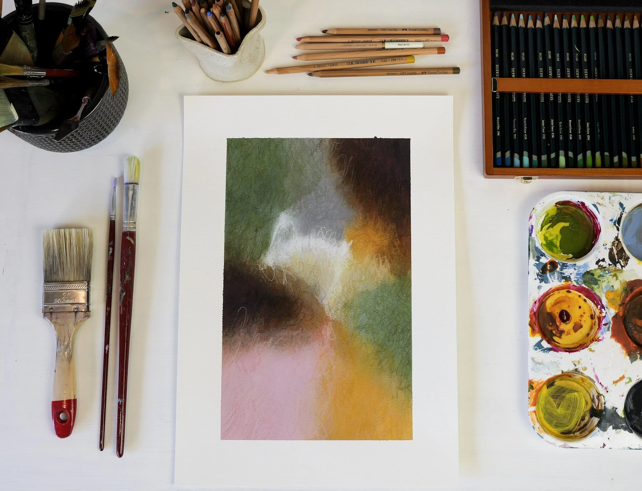 Painting supplies and a watercolor painting with blurred, abstract colors on a white table.