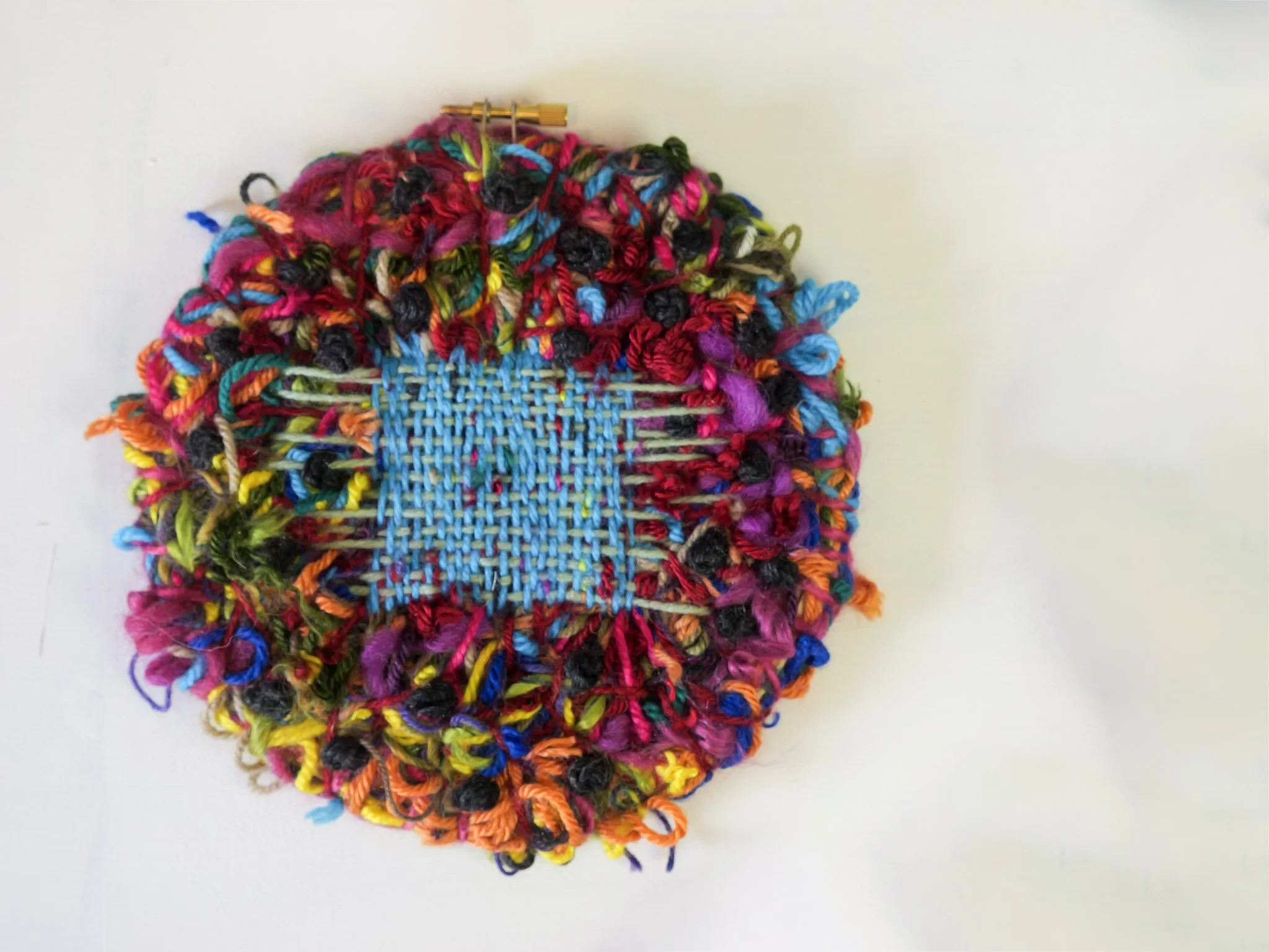 Colorful woven fabric surrounded by multicolored yarn and sewing pins.