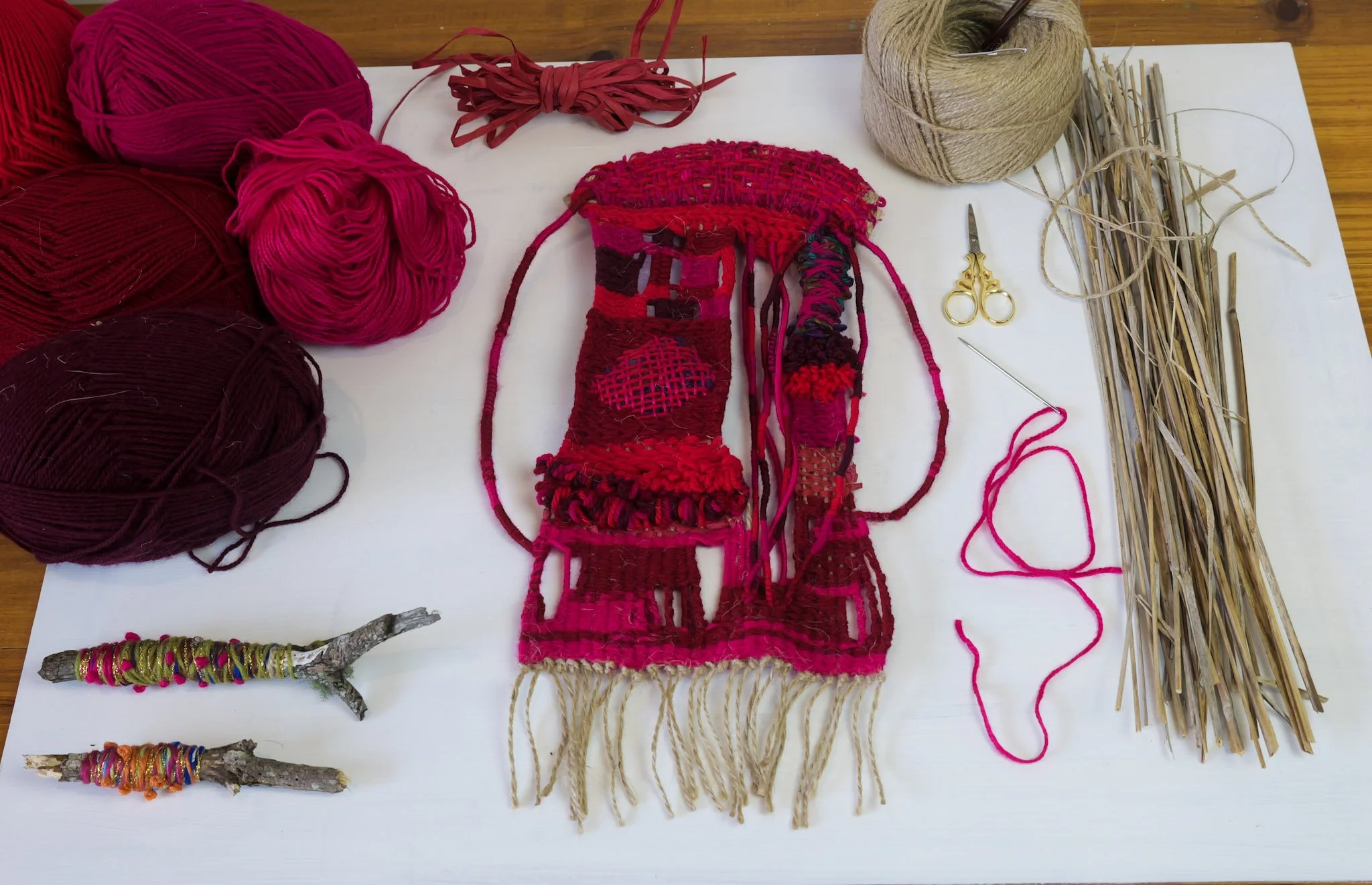 Various balls of red, pink, and brown yarn, knitting needles, scissors, and other knitting tools arranged on a white surface, with some projects in progress.