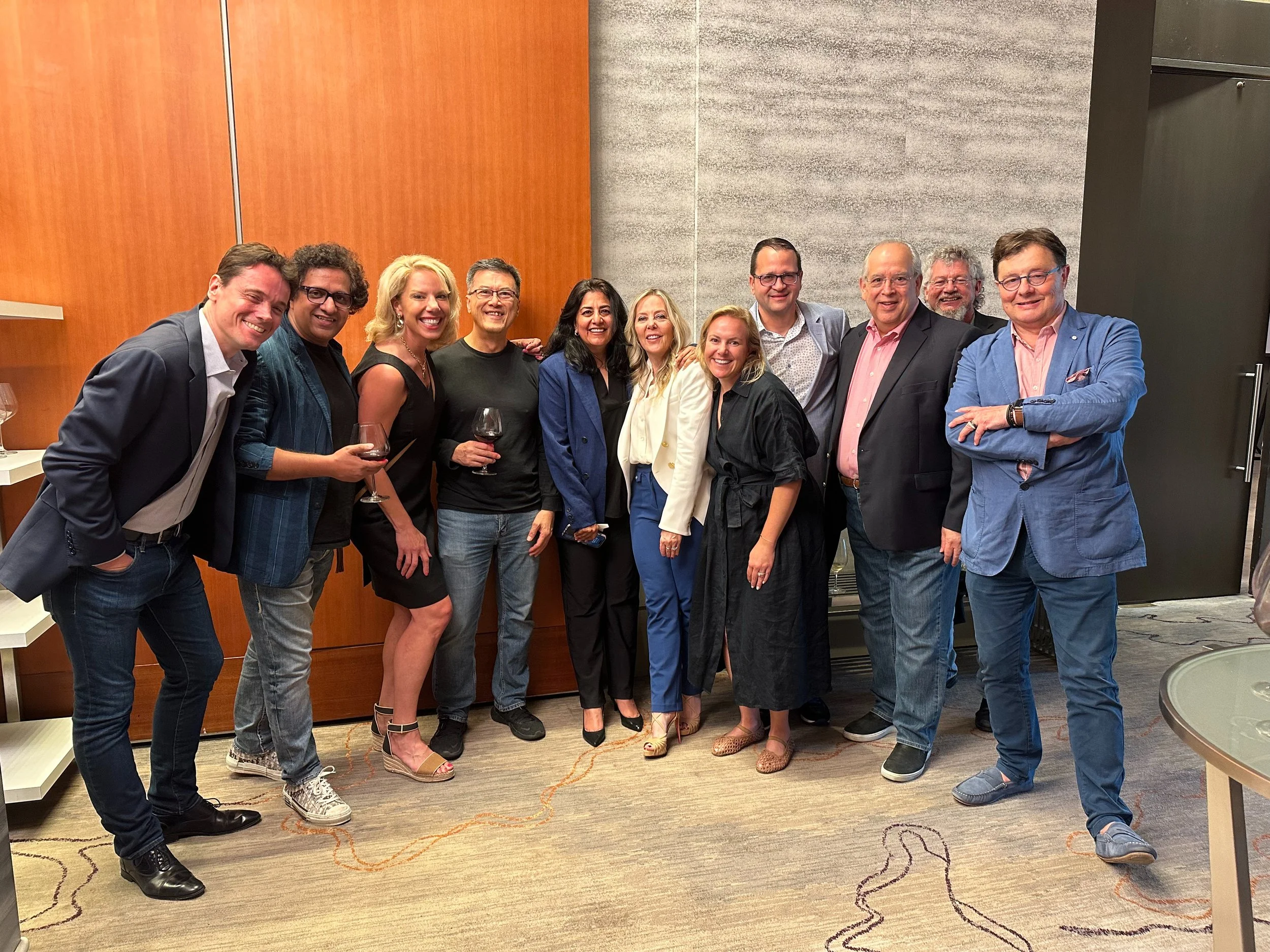 Group of eleven people dressed in business and casual attire, standing together in an indoor setting, smiling at the camera.