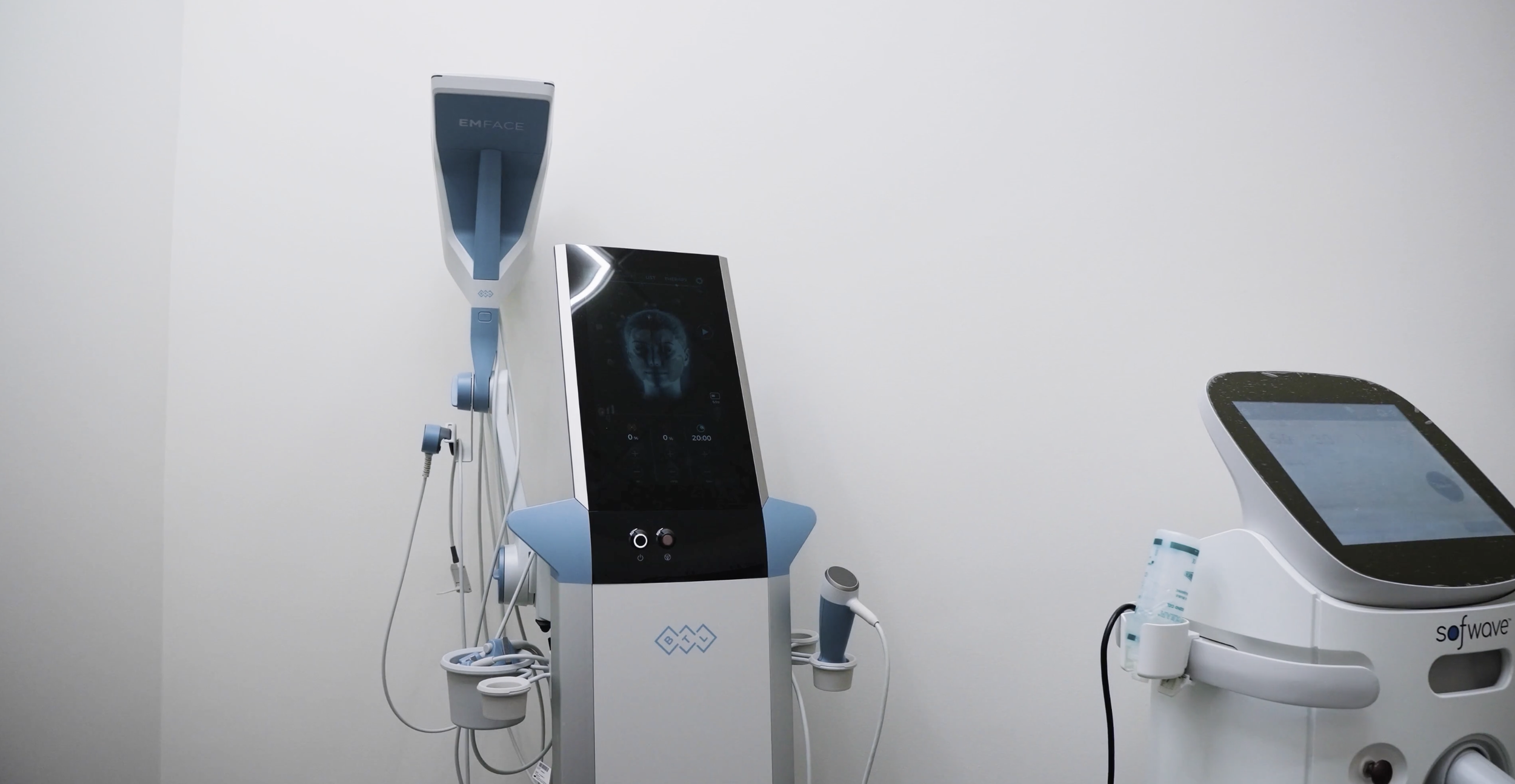 Medical examination room with two high-tech medical devices, including a large screen and various attachments, on white walls.