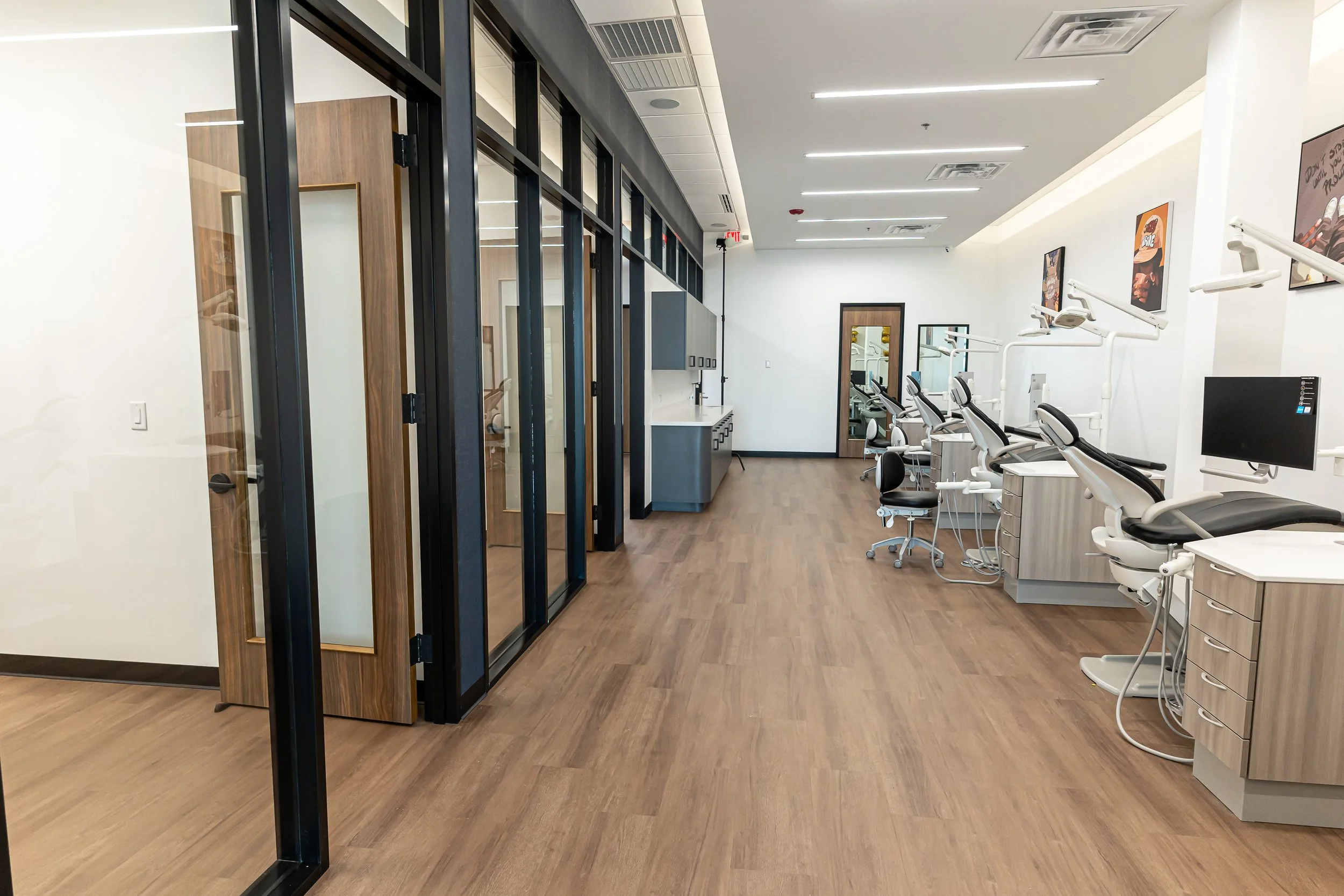 A modern dental clinic with dental chairs, computers, and cabinetry, separated by glass walls with wood frames.