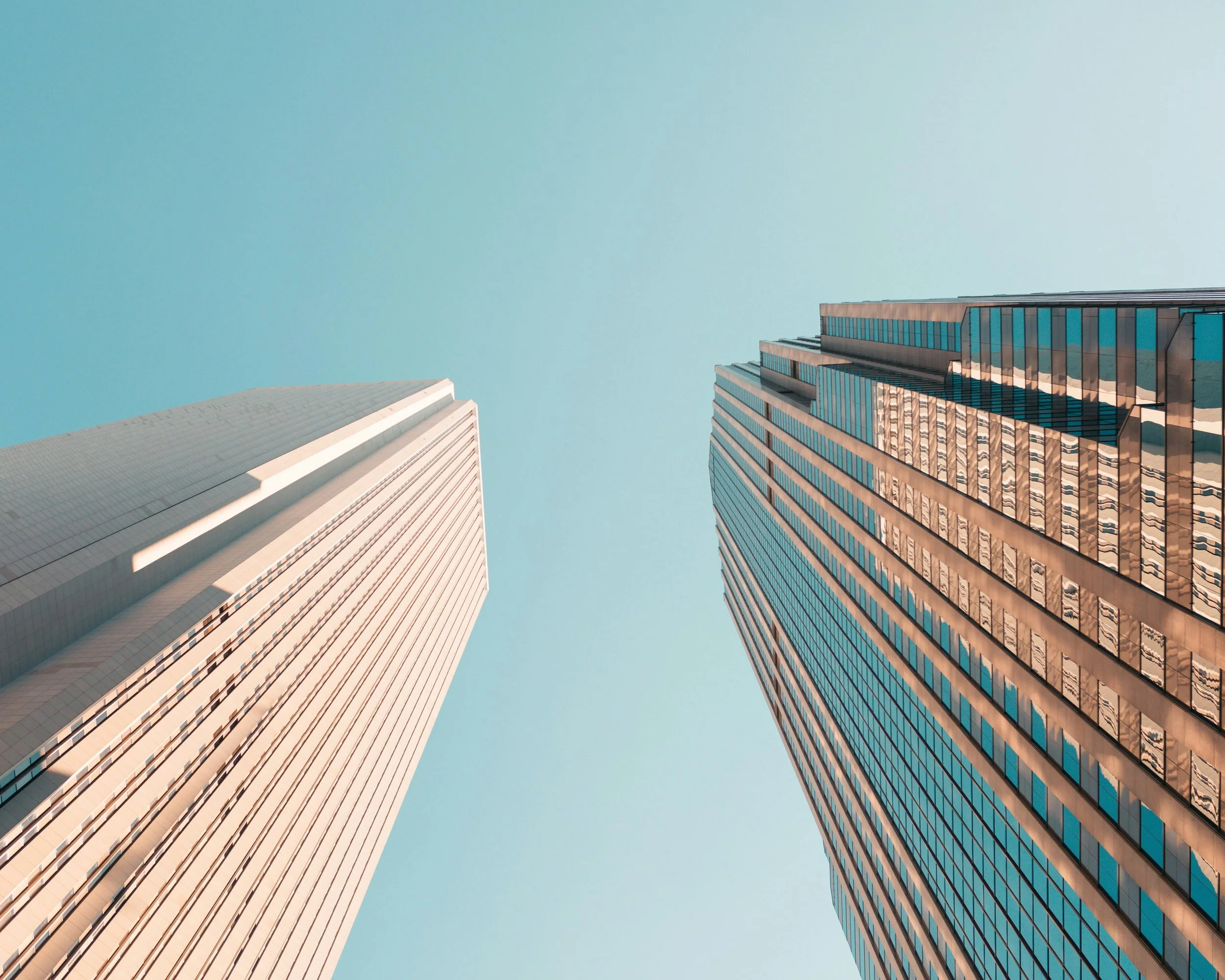 Two tall skyscrapers viewed from below against a clear blue sky.