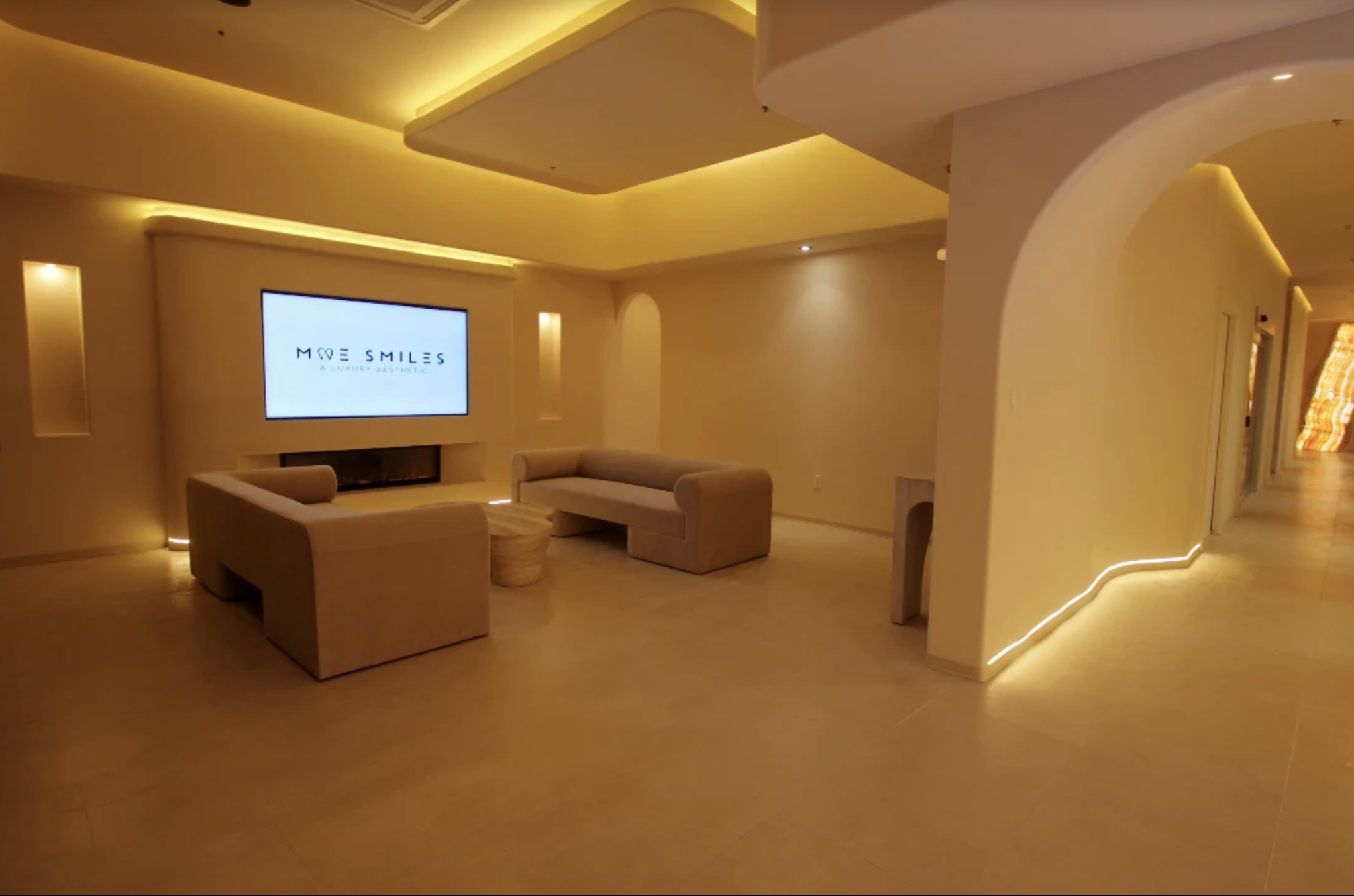 Modern, luxurious lounge area with beige sofas, a large digital screen reading 'More Smiles A Luxury Aesthetic,' and warm ambient lighting.