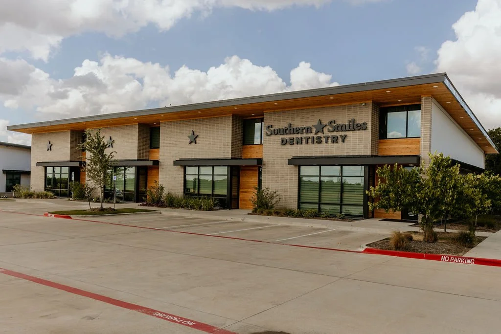 Exterior view of a modern two-story building labeled Southern Smiles Dentistry with a parking lot in front and a partly cloudy sky.