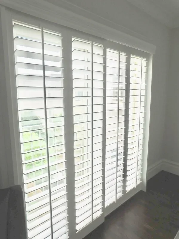 A set of white window shutters covering large glass windows in a room.