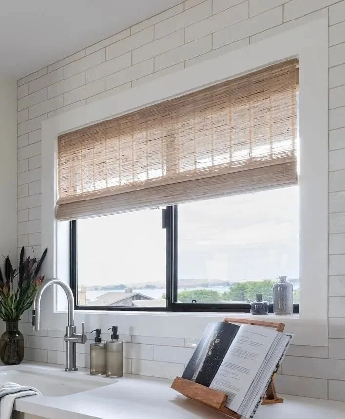Kitchen window with bamboo blind, white subway tile walls, a plant jar, soap dispensers, and an open book on a wooden stand.