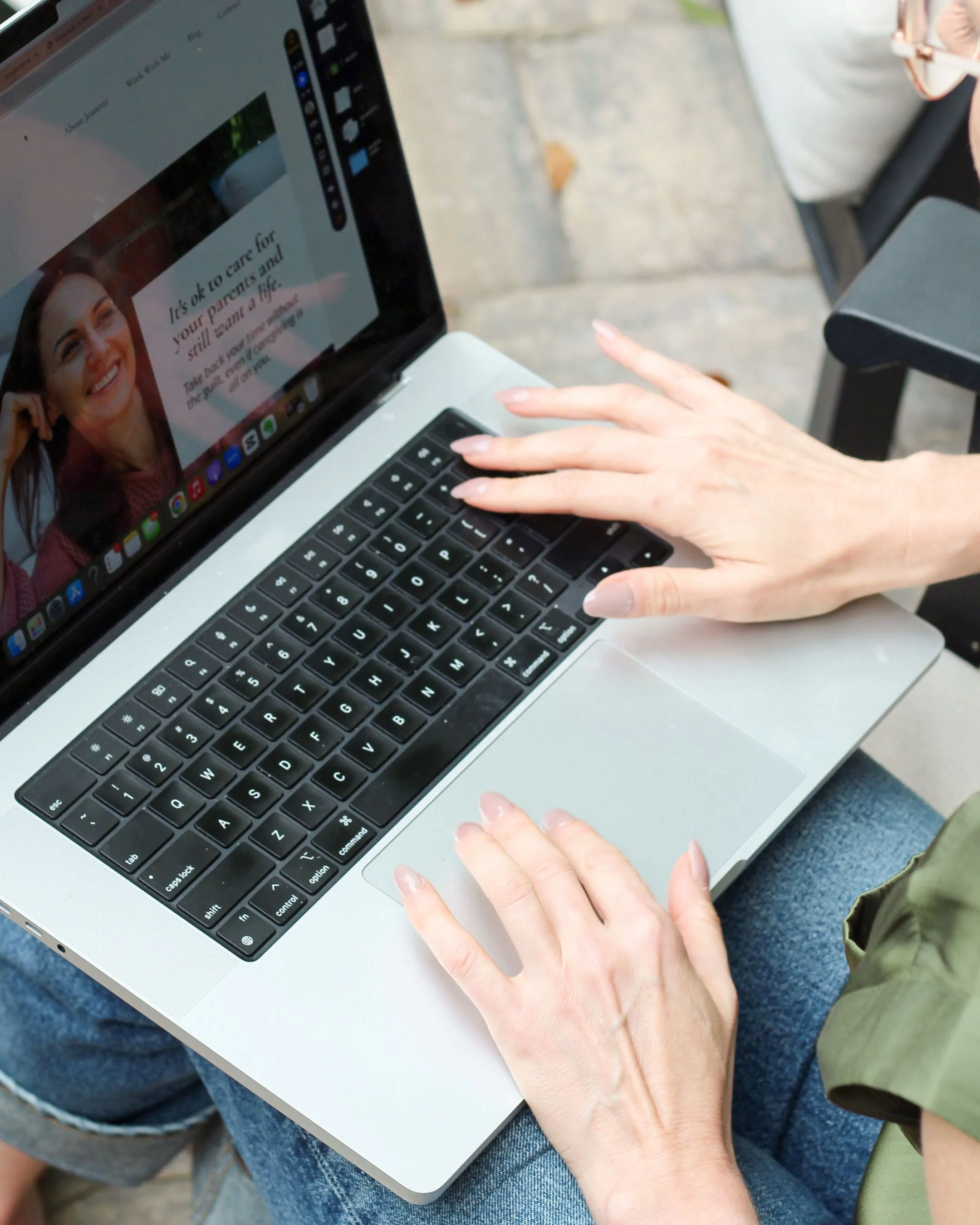 A person using a laptop with a black keyboard outdoors, with a webpage open showing a smiling woman's face and text about caring for parents.