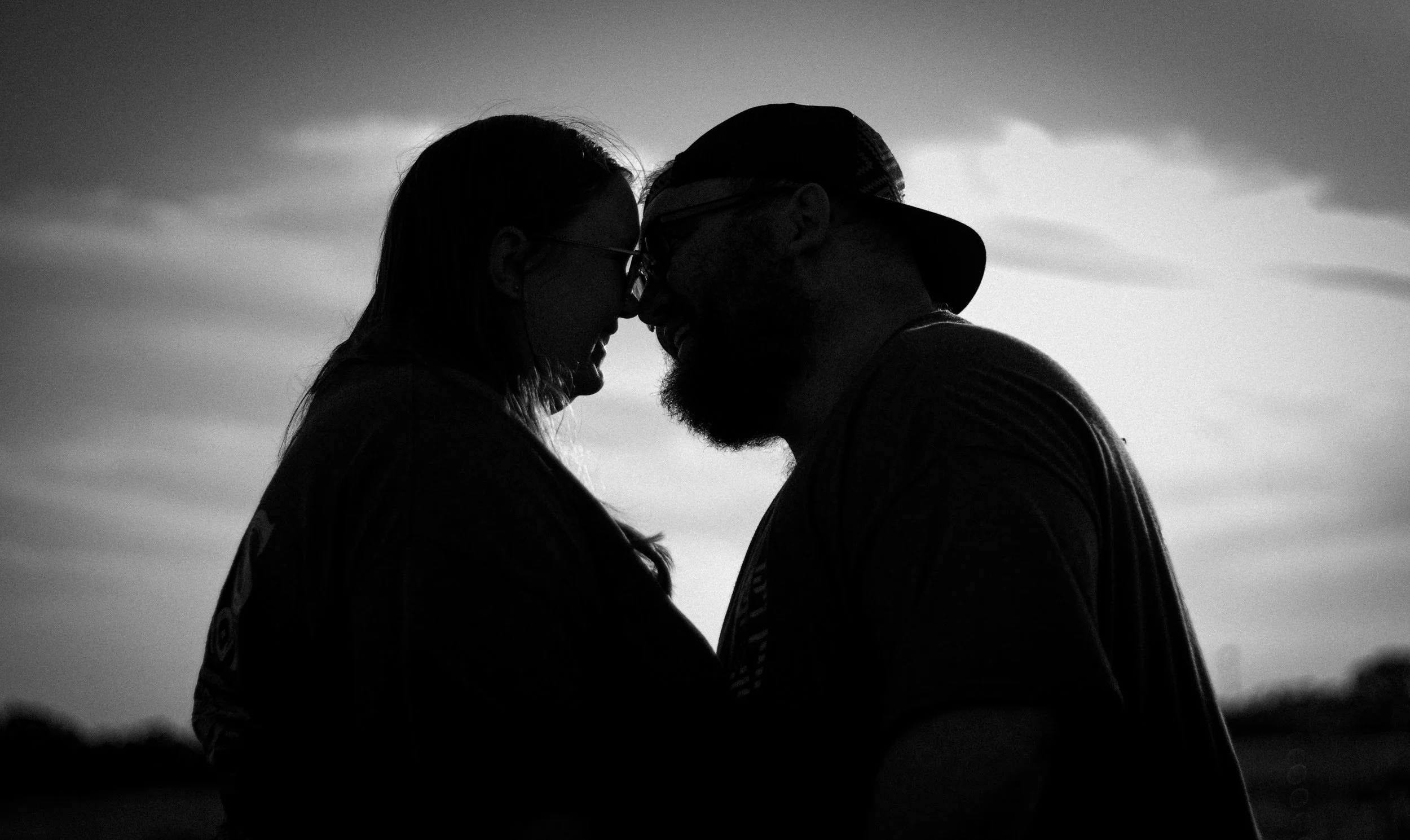 Silhouette of a couple with foreheads touching, smiling at each other during sunset.