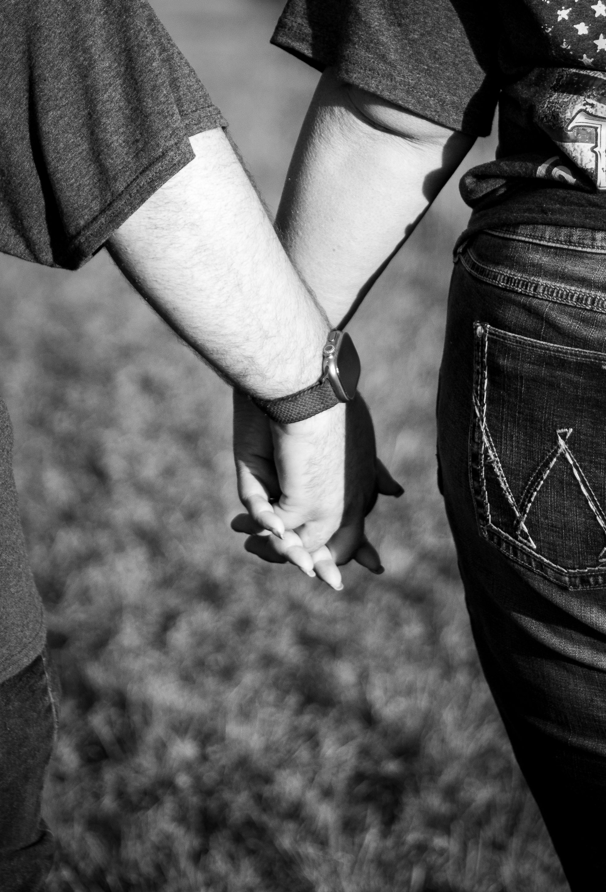 Two children holding hands outdoors, viewed from the waist up. The child on the left wears a short-sleeved shirt and a watch, while the child on the right wears a star-patterned shirt and jeans.