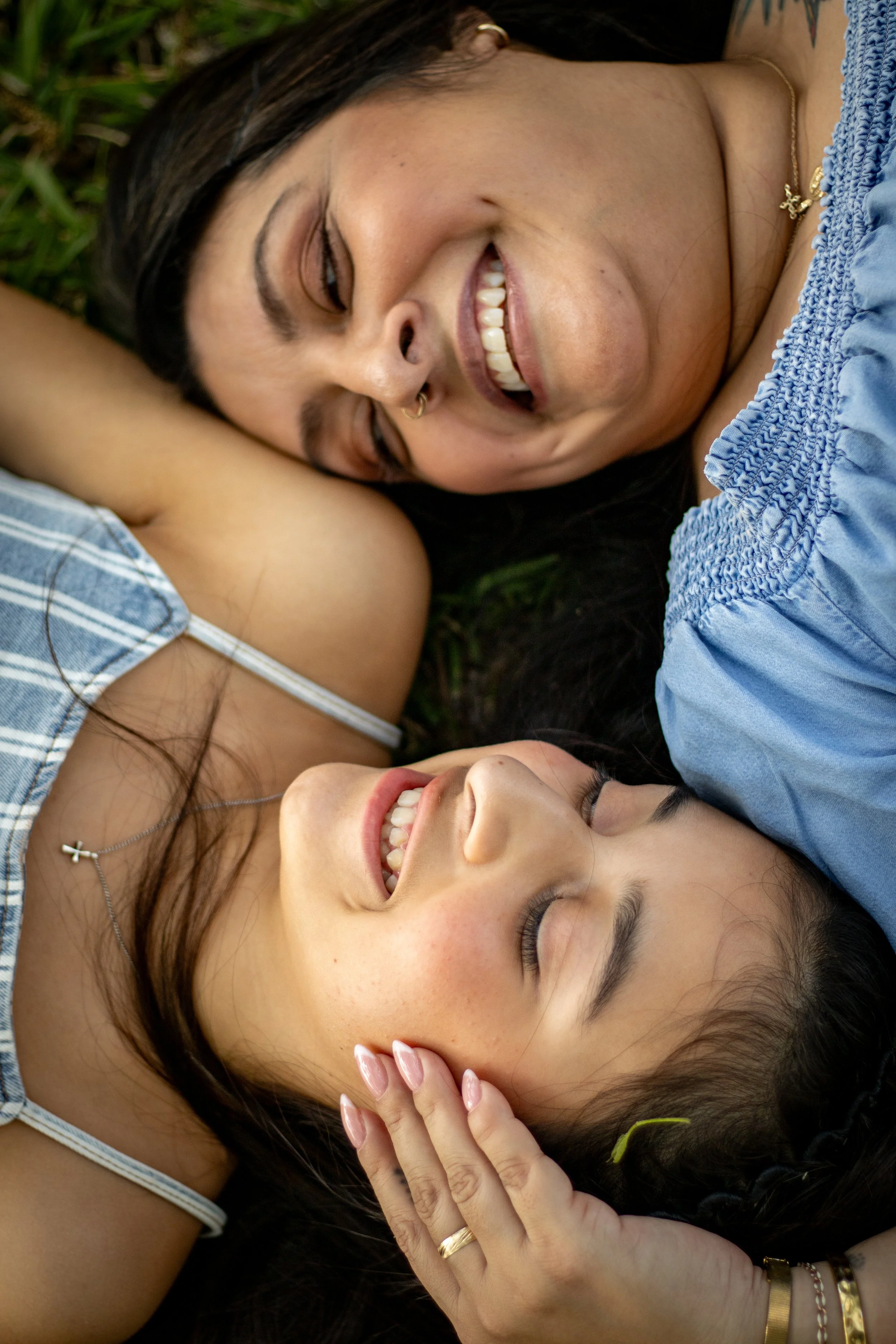 Two women lying on grass, smiling and looking at each other, close-up of their faces.
