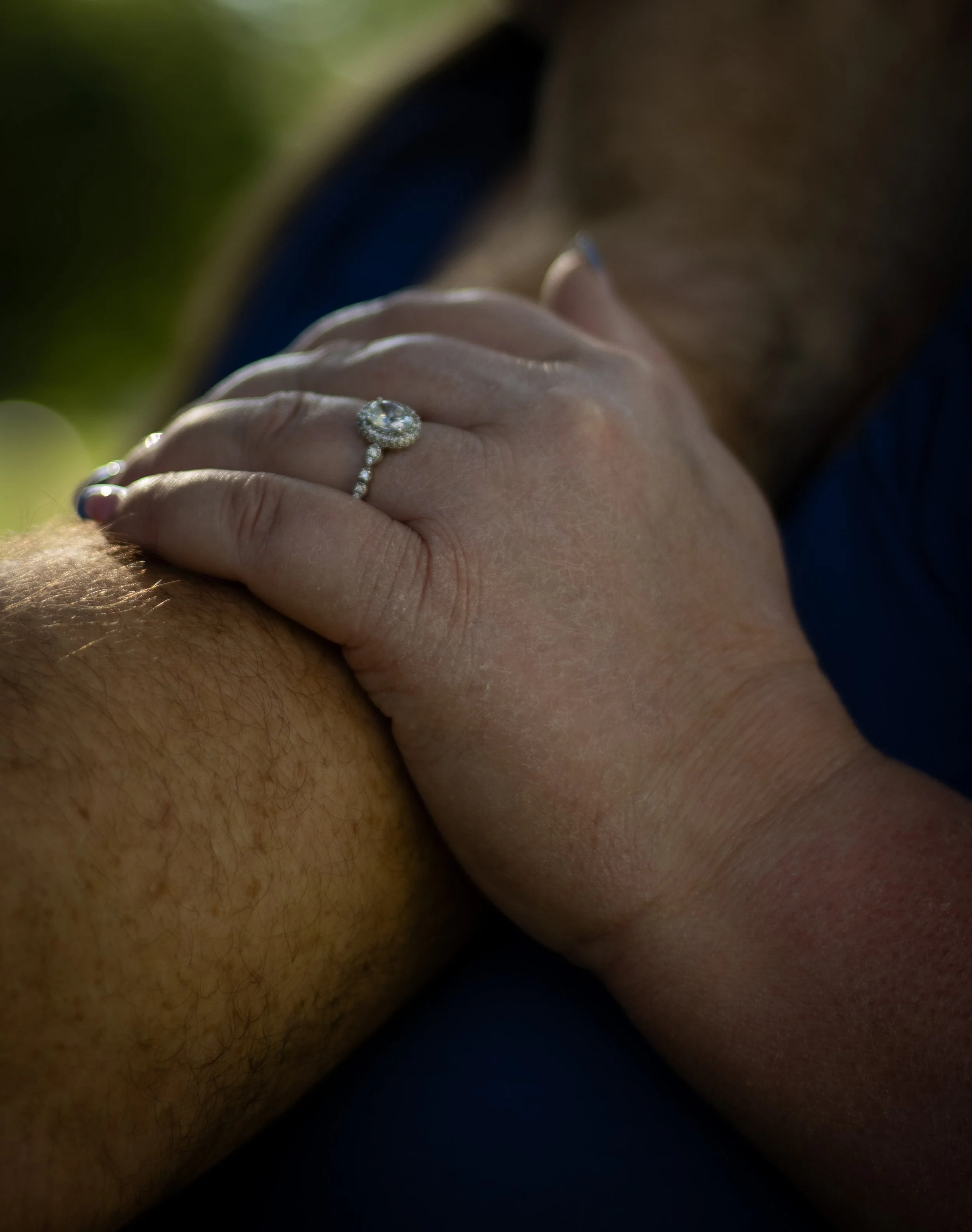 Close-up of a woman holding her hand with a diamond engagement ring, with blurred background.