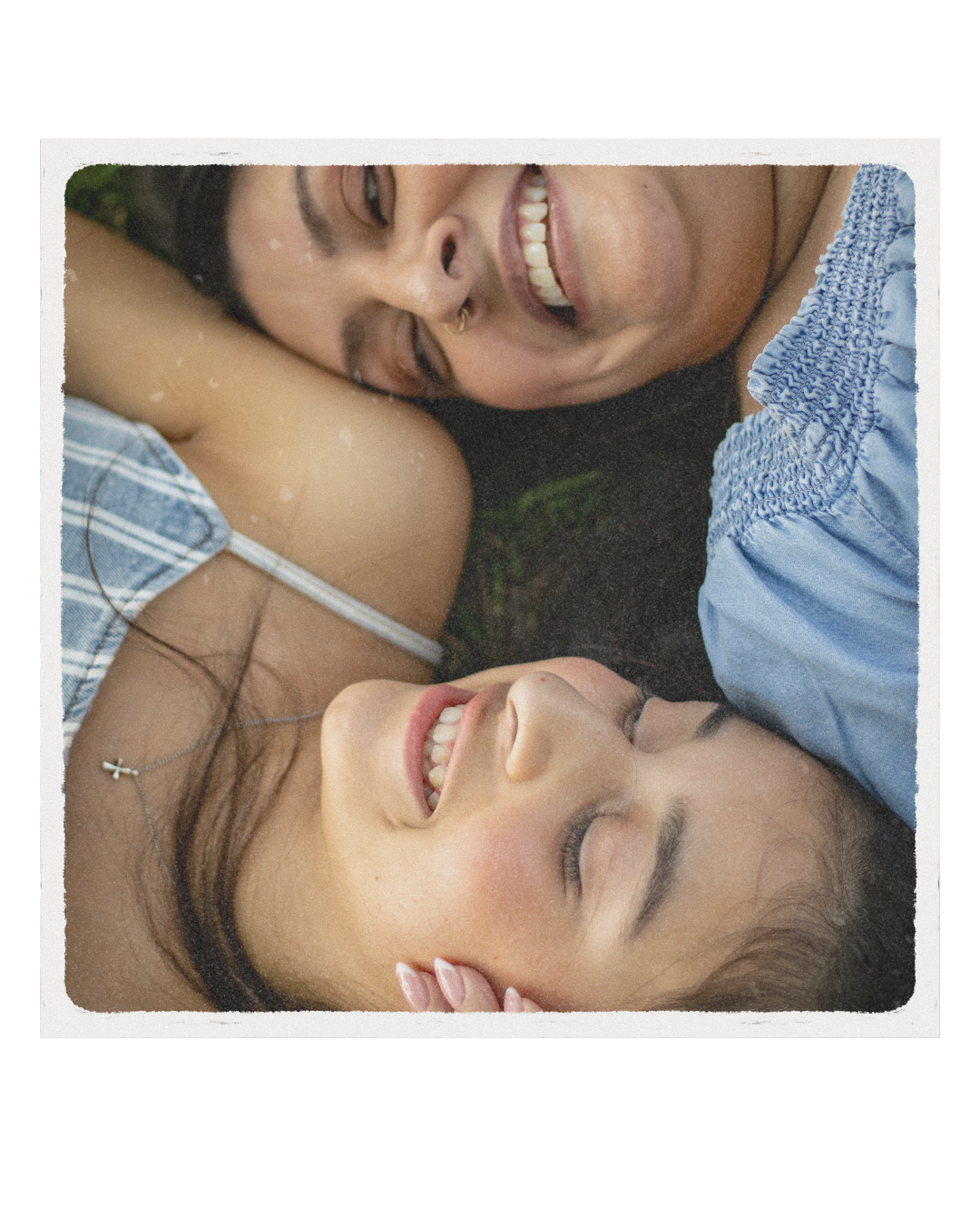 Two women lying on the ground, smiling and close to each other, with their heads touching.