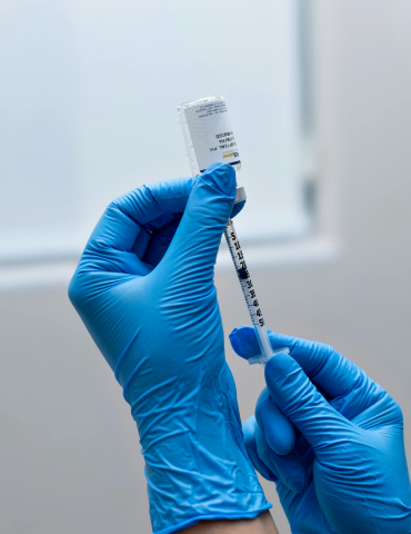 Hands wearing blue gloves preparing a syringe with a vaccine or medication.