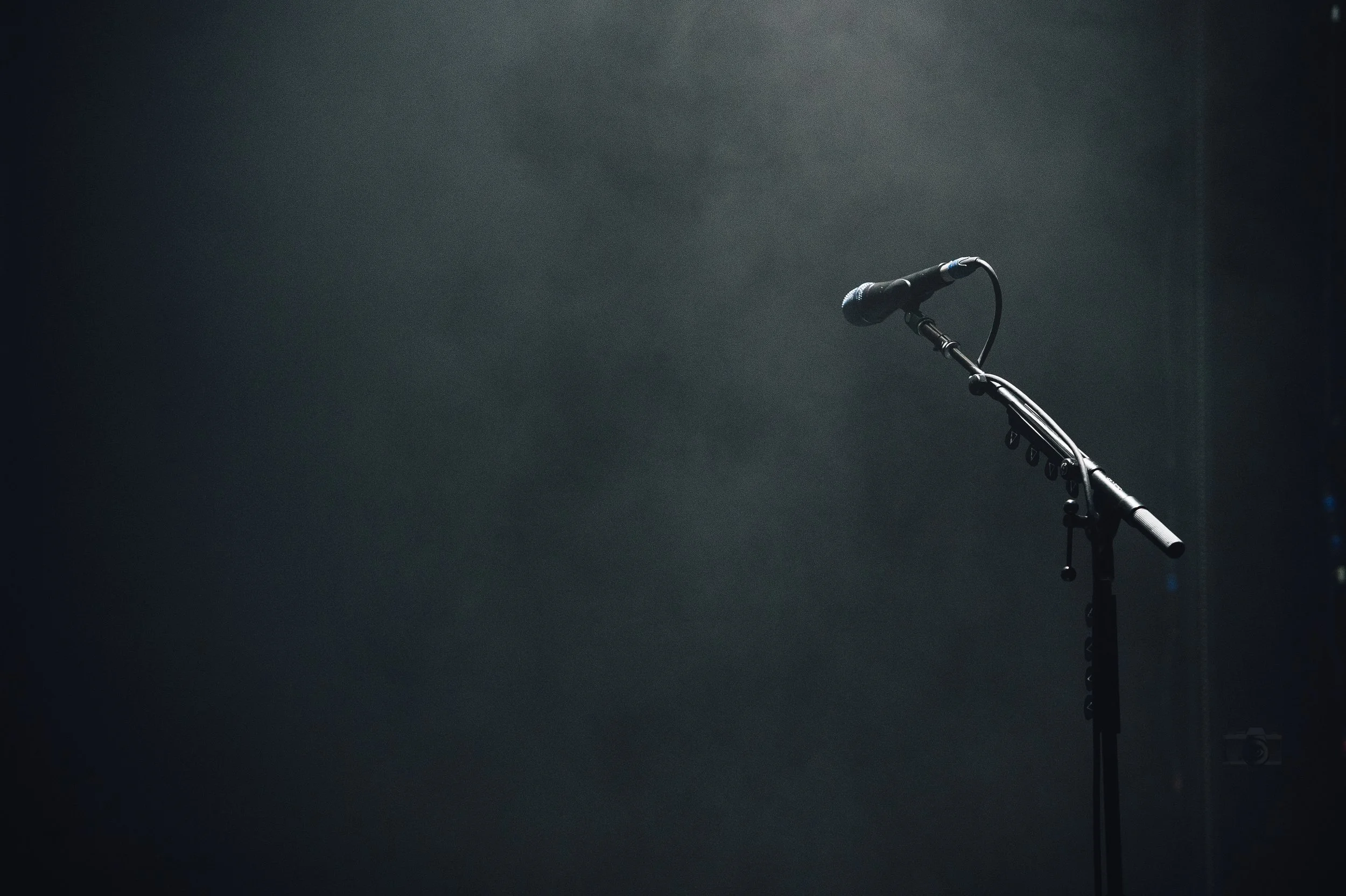 A microphone on a stand illuminated in a spotlight on a dark stage.