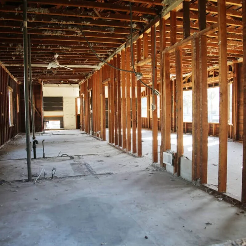 Interior of a building under construction with exposed wooden framing, temporary support poles, and open wall spaces.