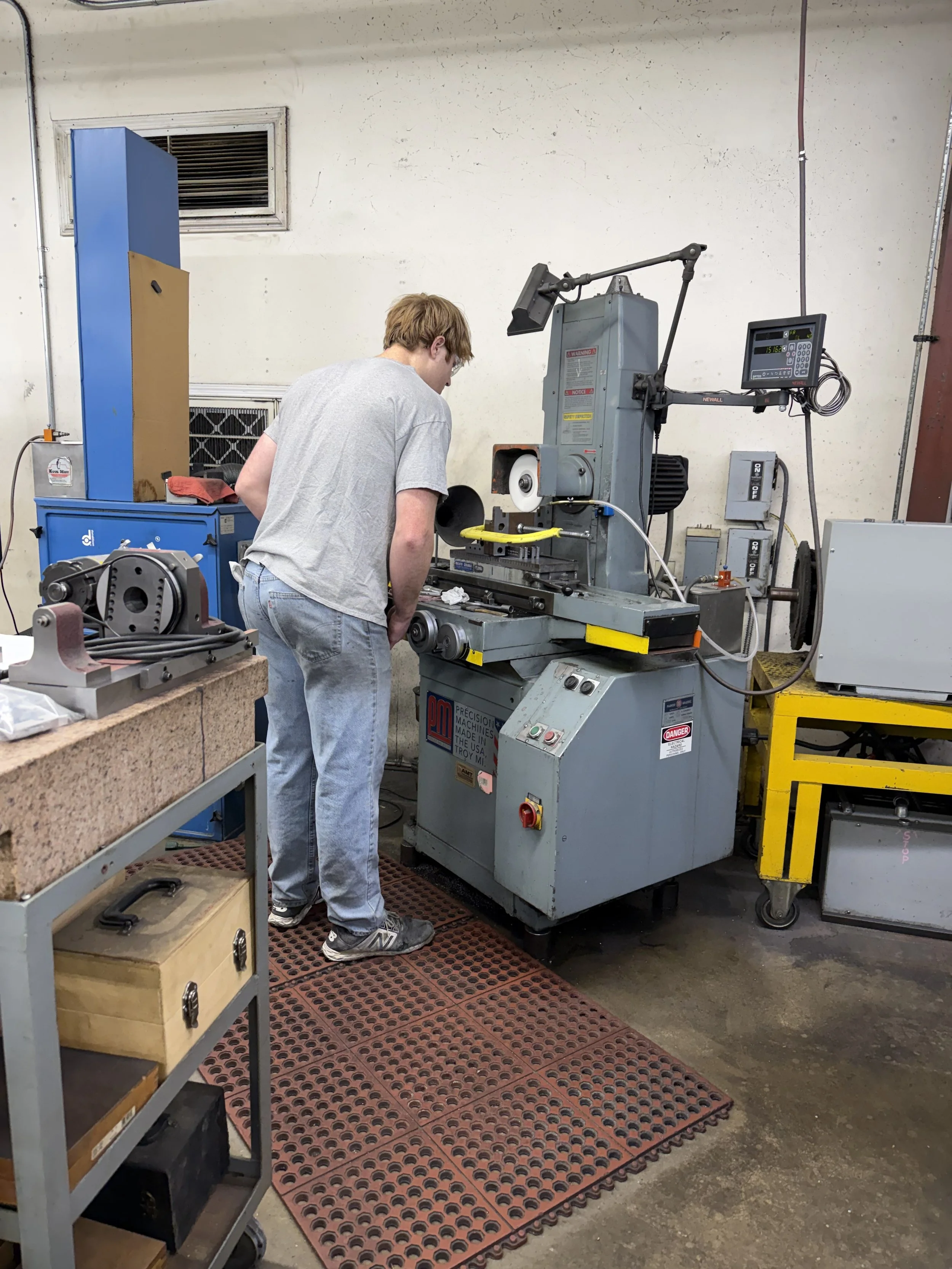 A person working with machinery in a workshop, focusing on a grey machine with controls and a digital display.