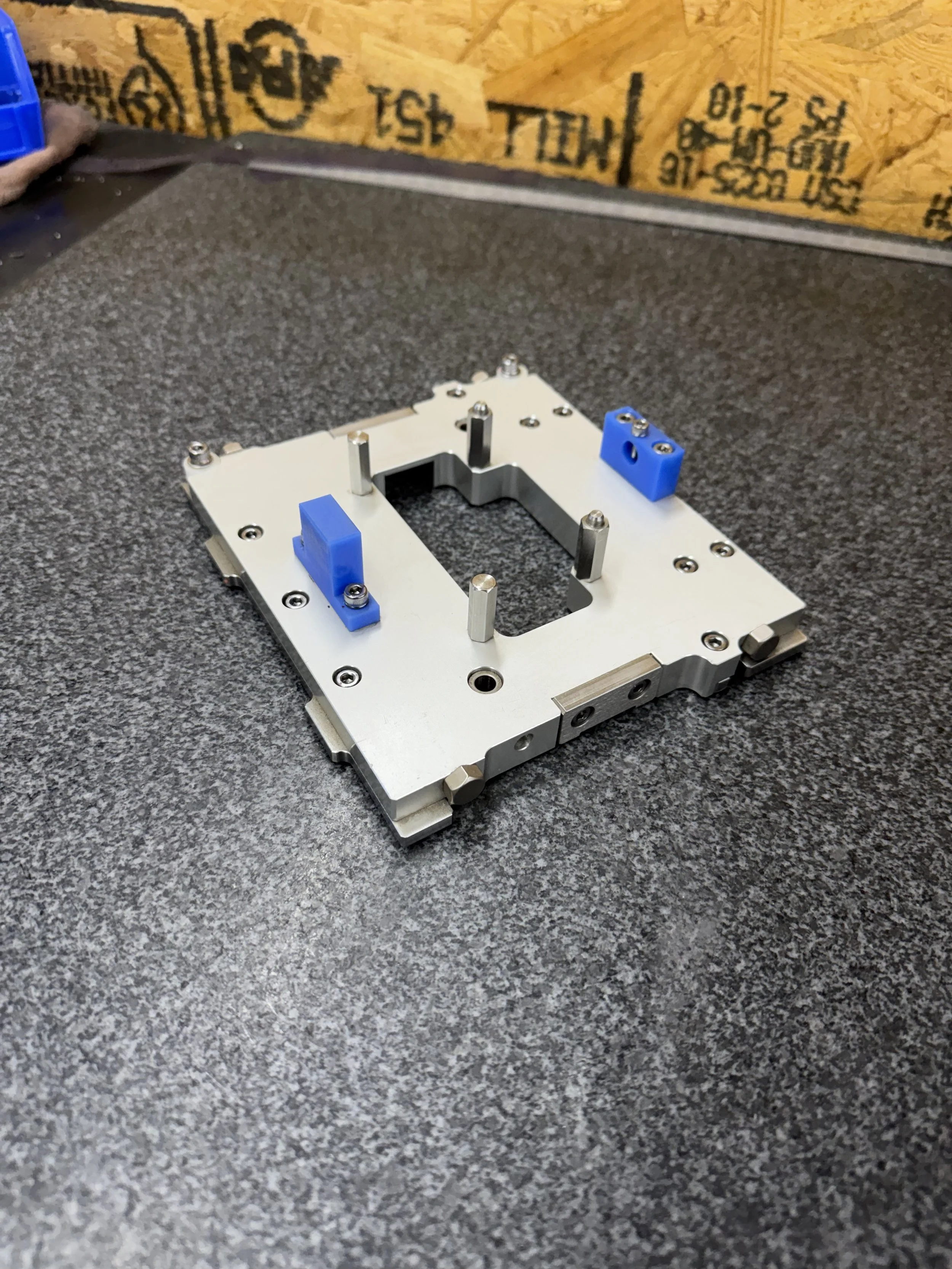 Metal mechanical component with blue plastic parts and multiple screws on a dark textured work surface.