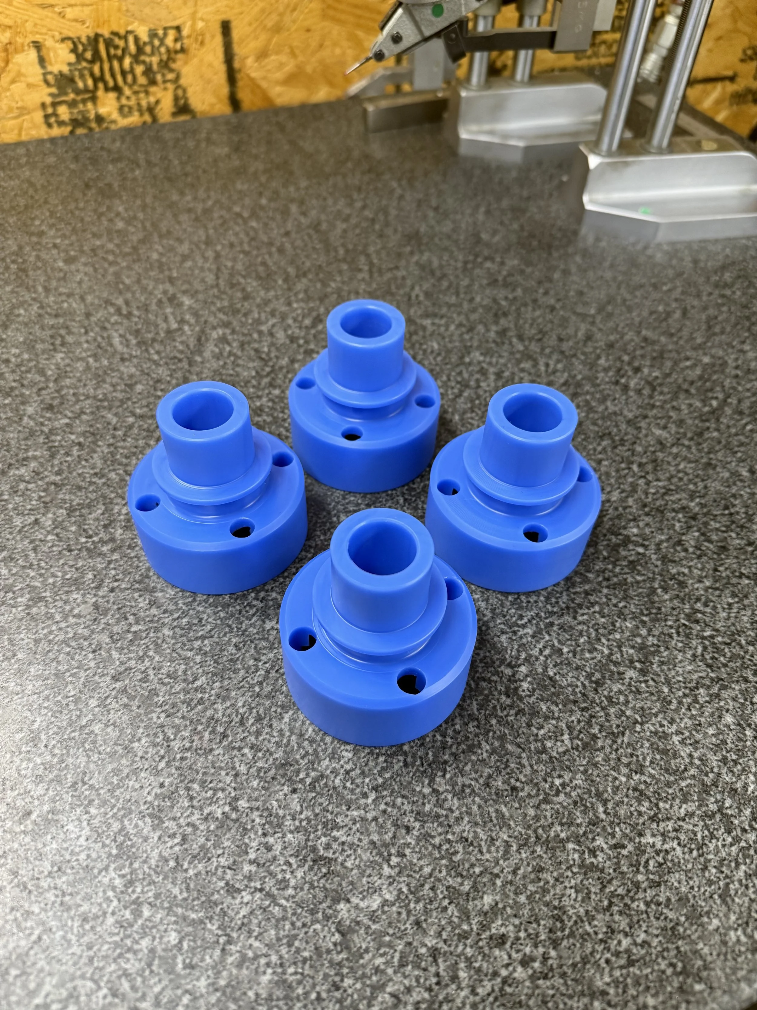 Four blue plastic machined parts with holes, arranged in a cluster on a gray work surface.