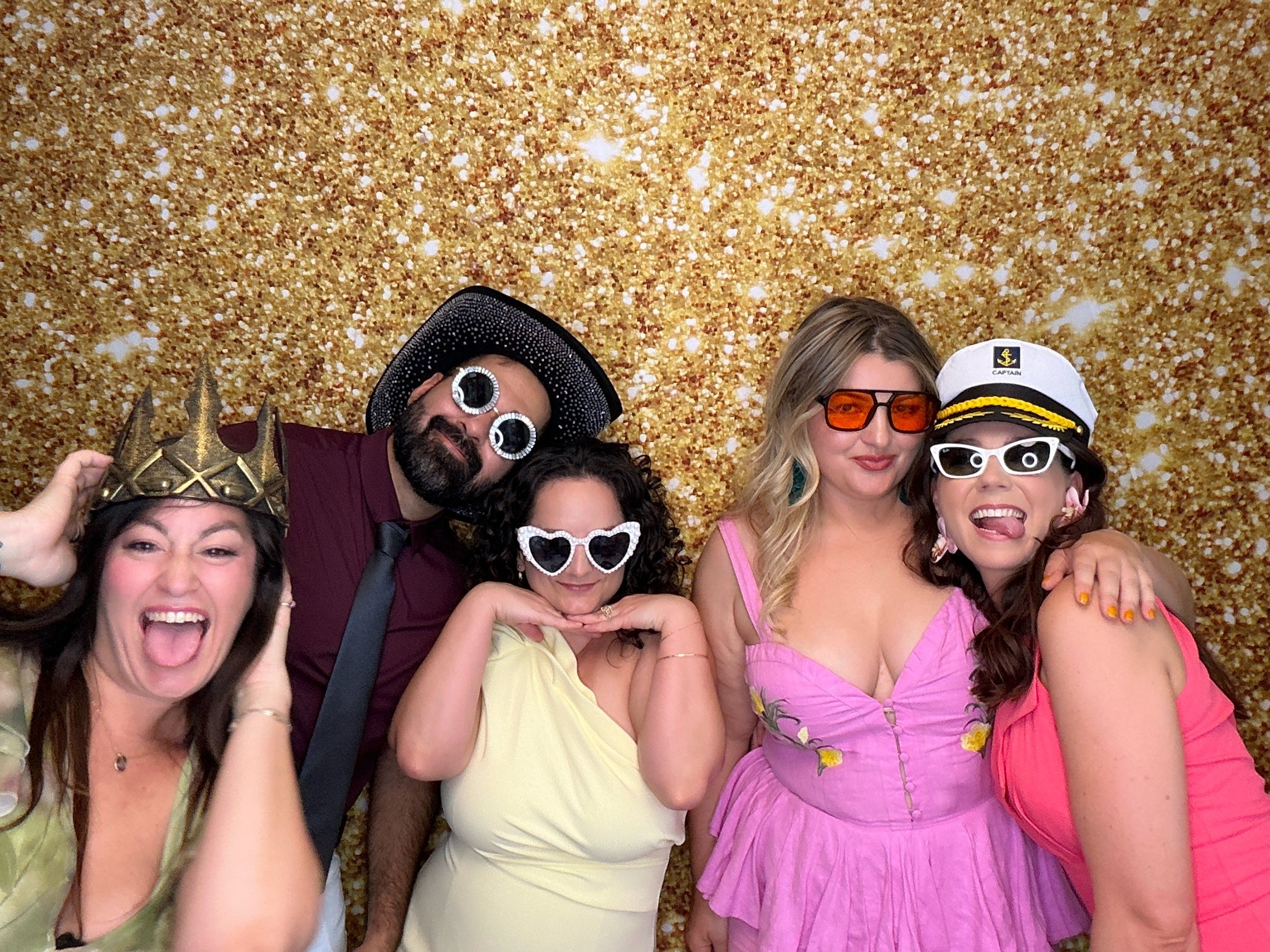 Guests posing with fun party props at an Orlando Photo Booth rental featuring a gold glitter backdrop by Pop & Pose Events.