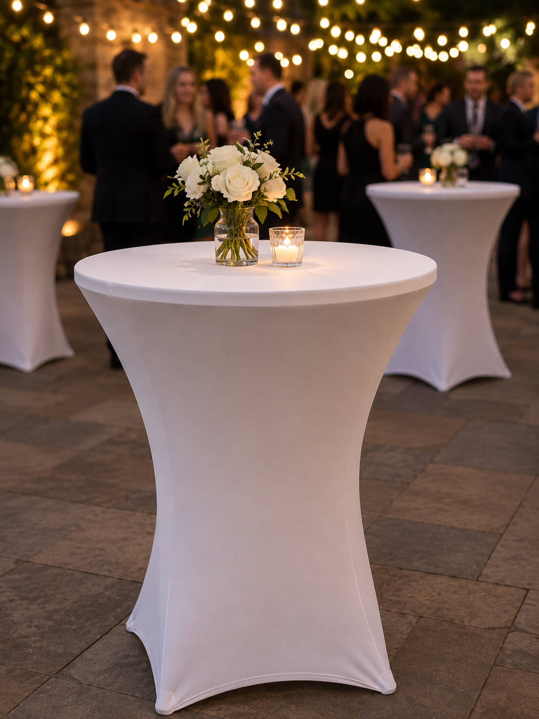 30-inch white cocktail table with fitted linen at an elegant wedding cocktail hour, featuring a floral centerpiece, candle, and guest mingling beneath the ring lights in Winter Park, Florida.