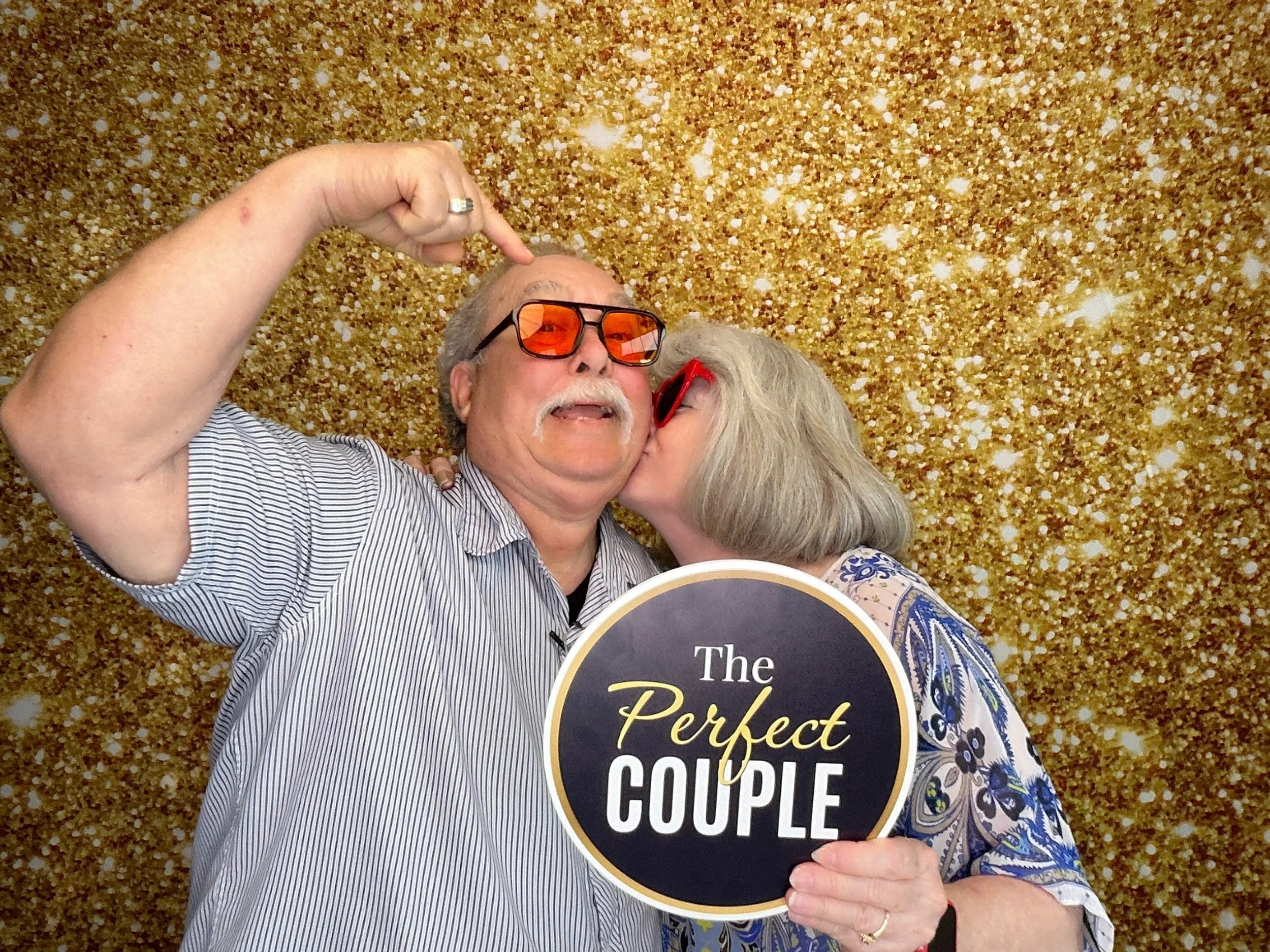 Fun wedding Photo Booth moment with custom props and gold glitter backdrop by Pop & Pose Events in Central Florida.