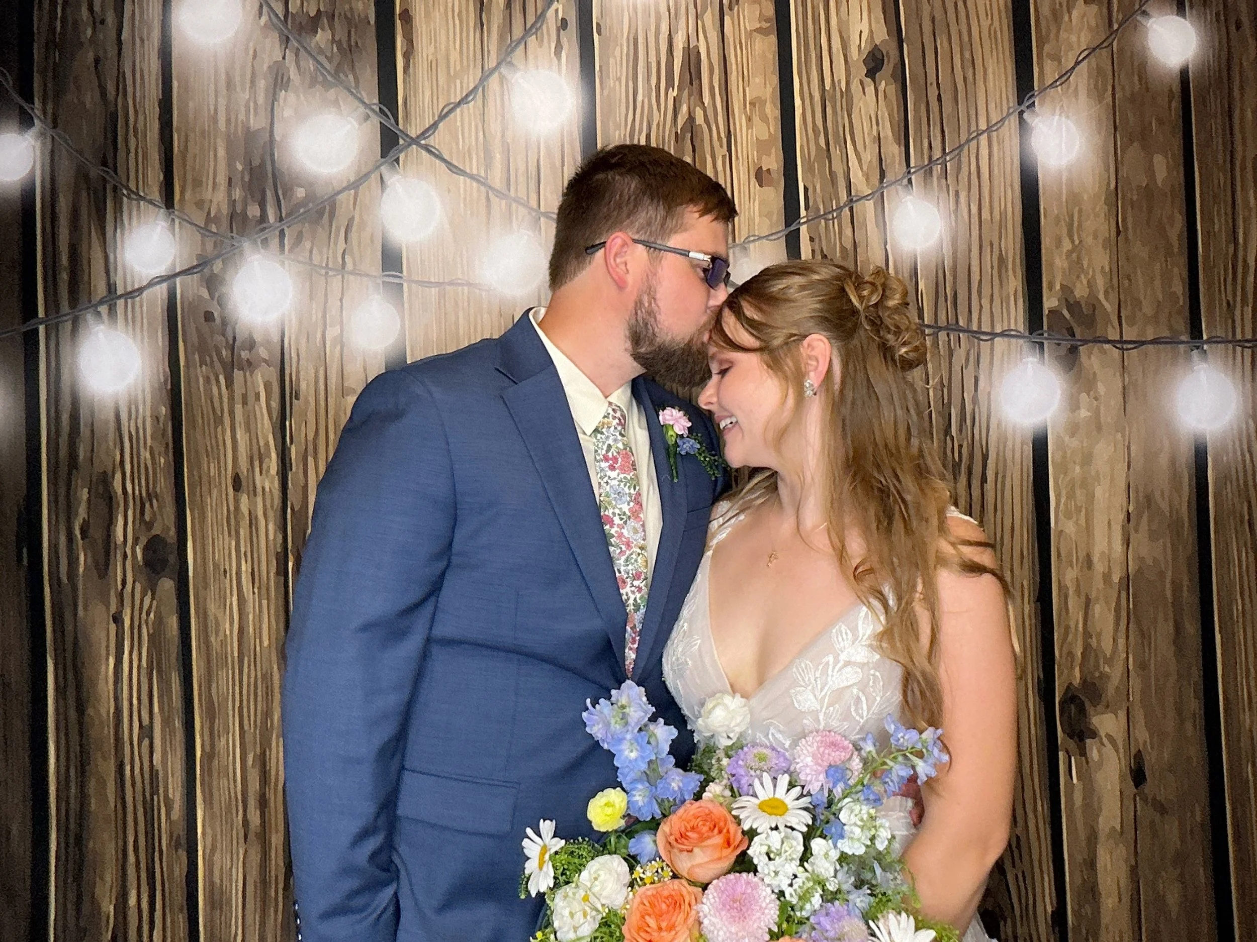 A bride and groom share a kiss in the Photo Booth at their wedding reception in front of a wood backdrop with spring lights in Apopka, Florida.