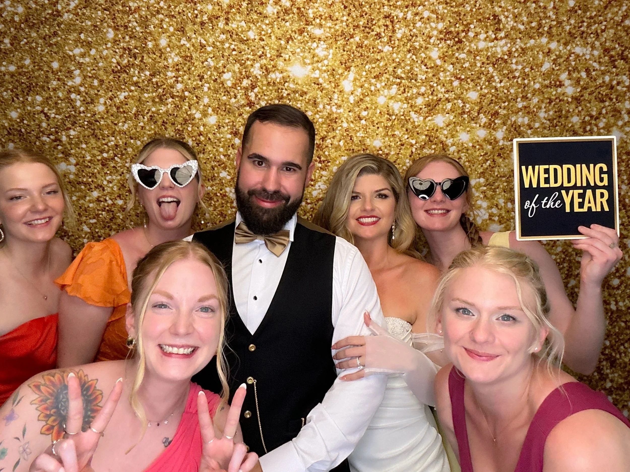 Wedding guests enjoying the Pop & Pose Events Photo Booth with fun props and a gold glitter backdrop at a Central Florida wedding reception.