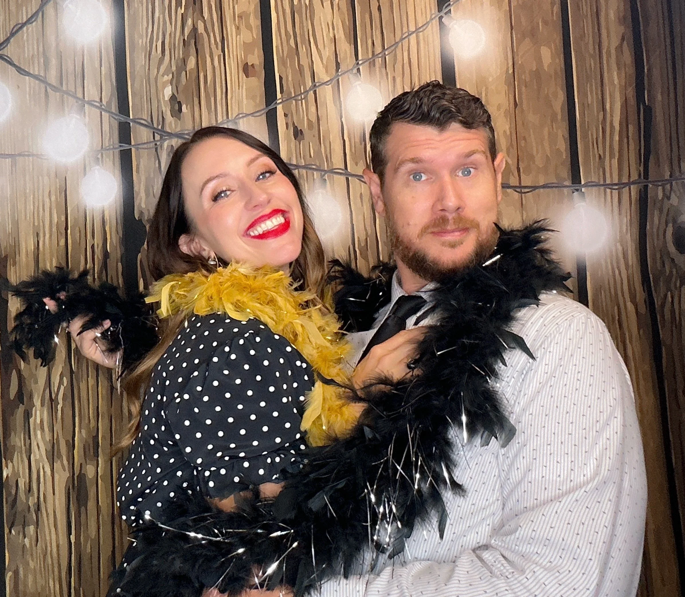 Guests celebrating with fun props at an Orlando Photo Booth rental featuring a wood backdrop with string lights.