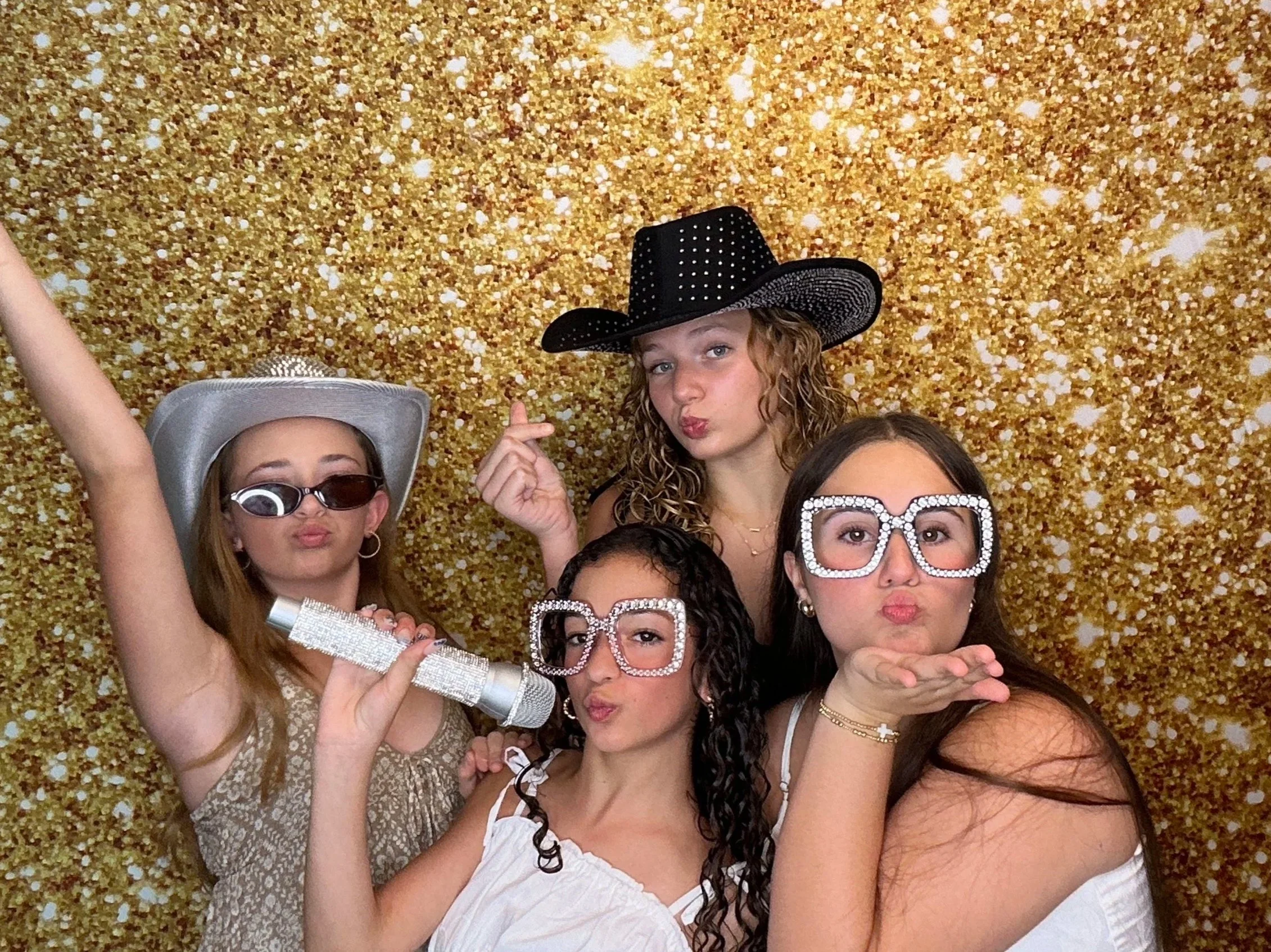 Friends celebrating with fun Photo Booth props infront of a gold glitter backdrop at a special event. Pop & Pose provides premium Photo Booth rentals for weddings, birthdays, and celebrations throughout Oviedo, Apopka, Orlando, & Central Florida.
