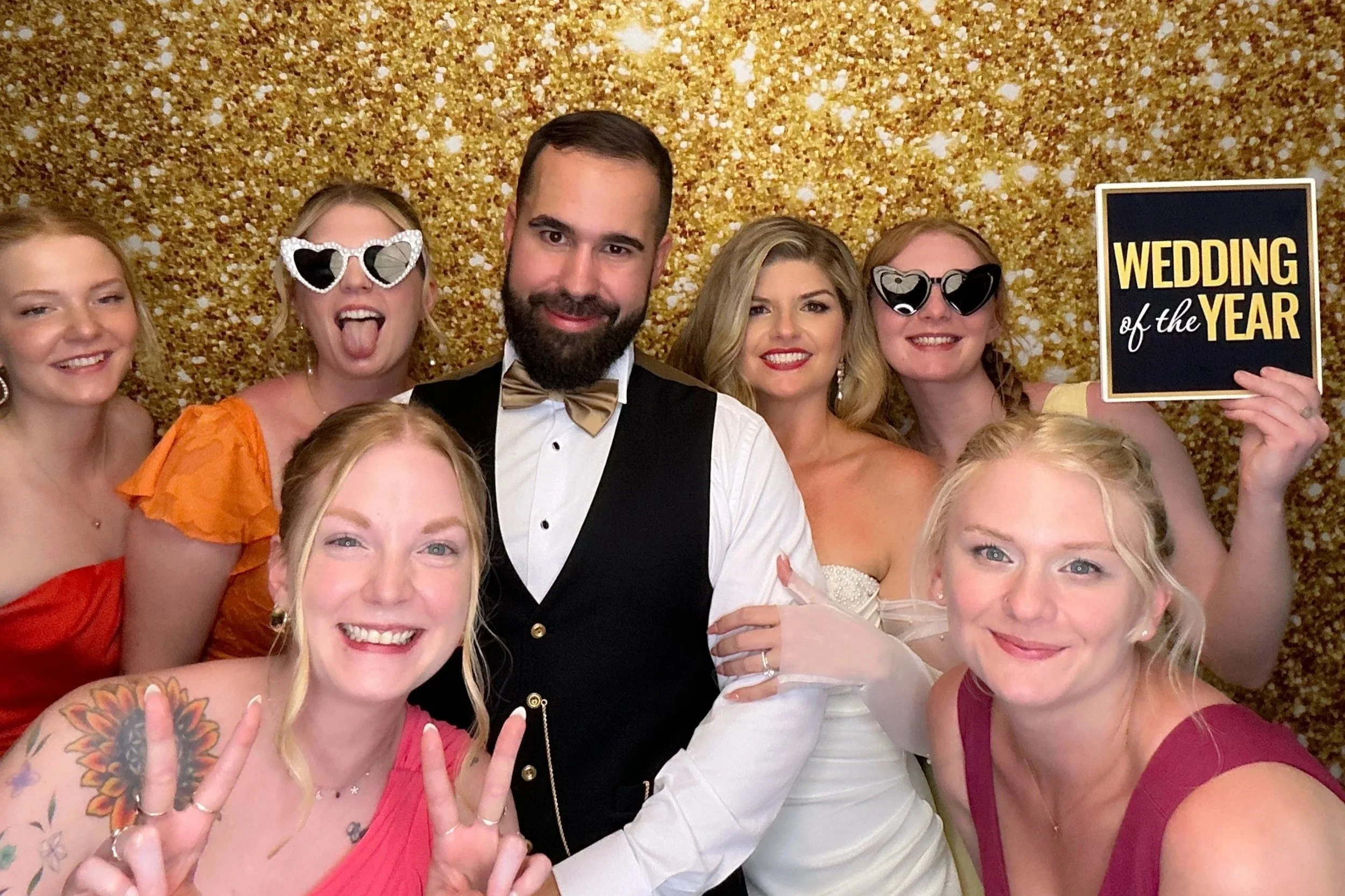 Guests enjoying a modern Photo Booth at a wedding in Orlando, Florida, posing in front of a gold sequin backdrop with fun props and signs.