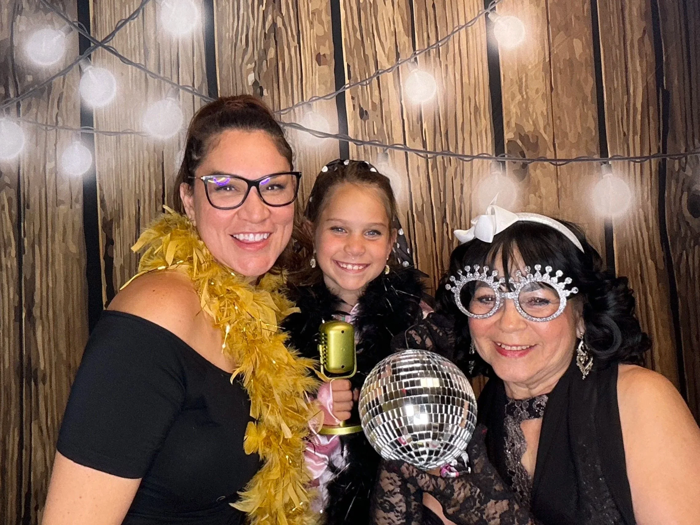 Guests celebrating a milestone birthday with fun Photo Booth props in front of a rustic wood backdrop with string lights. Pop & Pose Events offers Photo Booth rentals for birthday parties and private events throughout Sanford & Orlando.