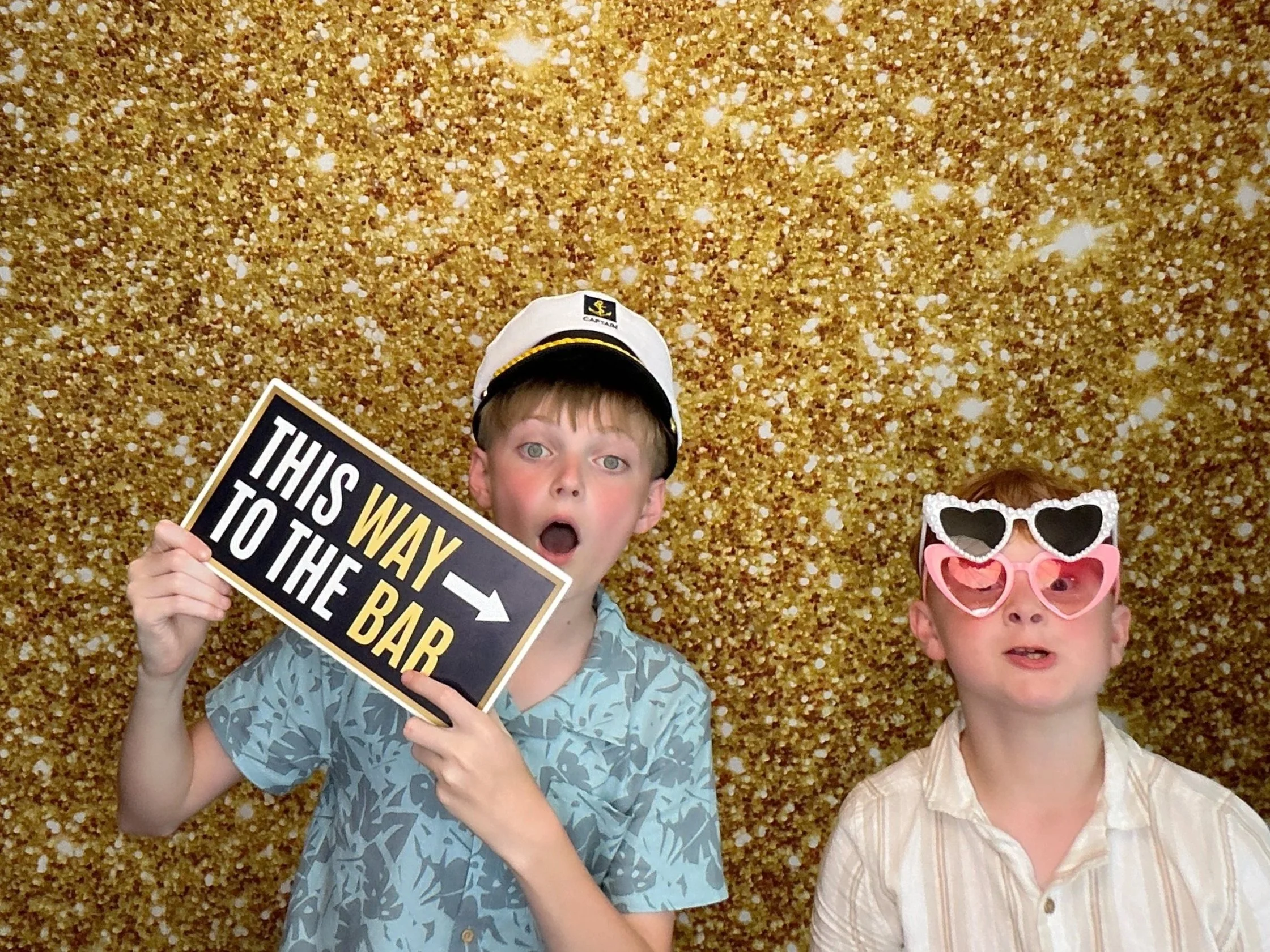 Two children enjoying a Pop & Pose Events Photo Booth with fun props and a gold glitter backdrop at a birthday party. Our Orlando Photo Booth rentals create unforgettable memories for birthdays, school events, and celebrations across Central Florida.