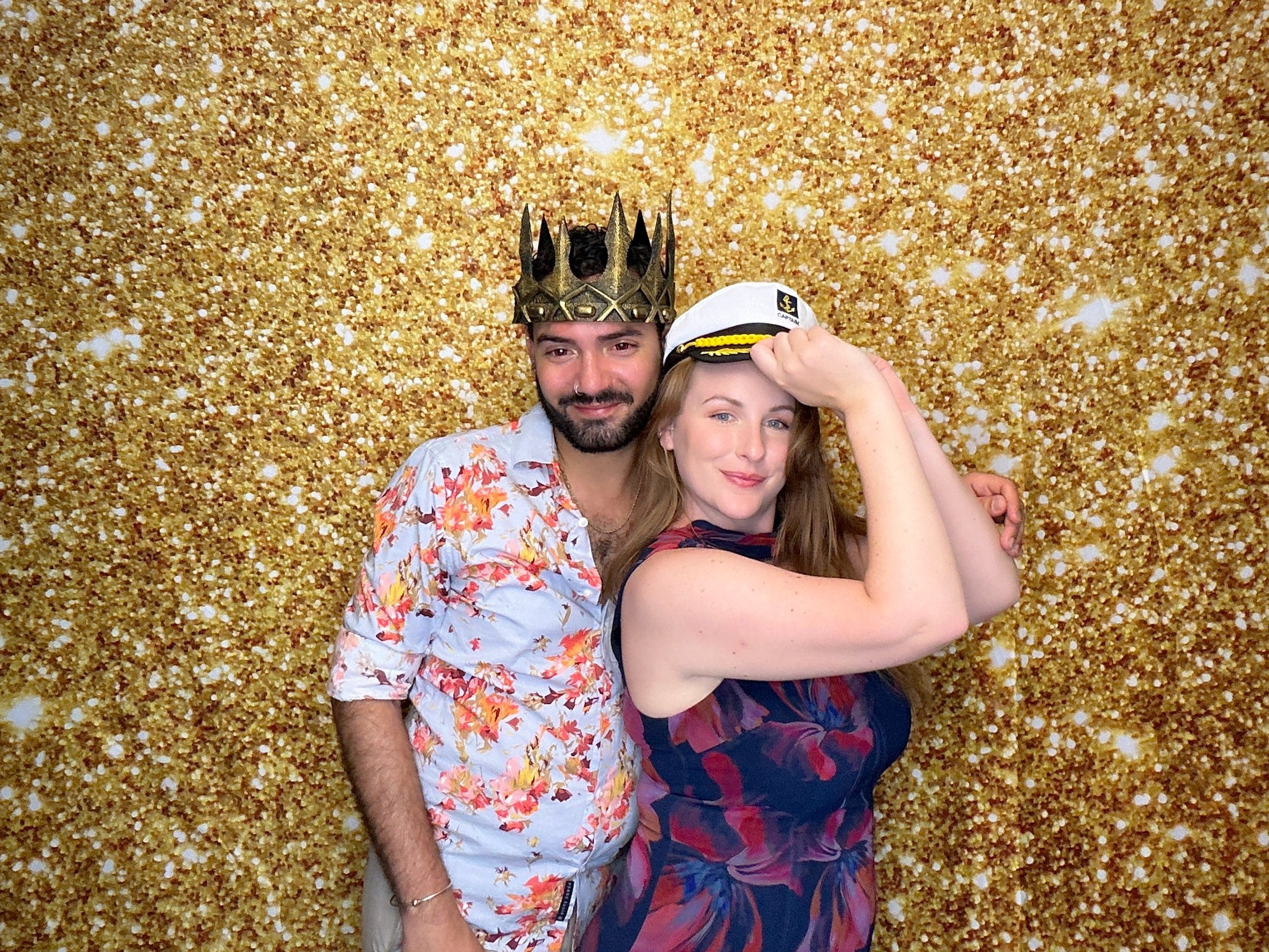 Couple enjoying a custom Photo Booth experience with themed props and gold backdrop by Pop & Pose Events.