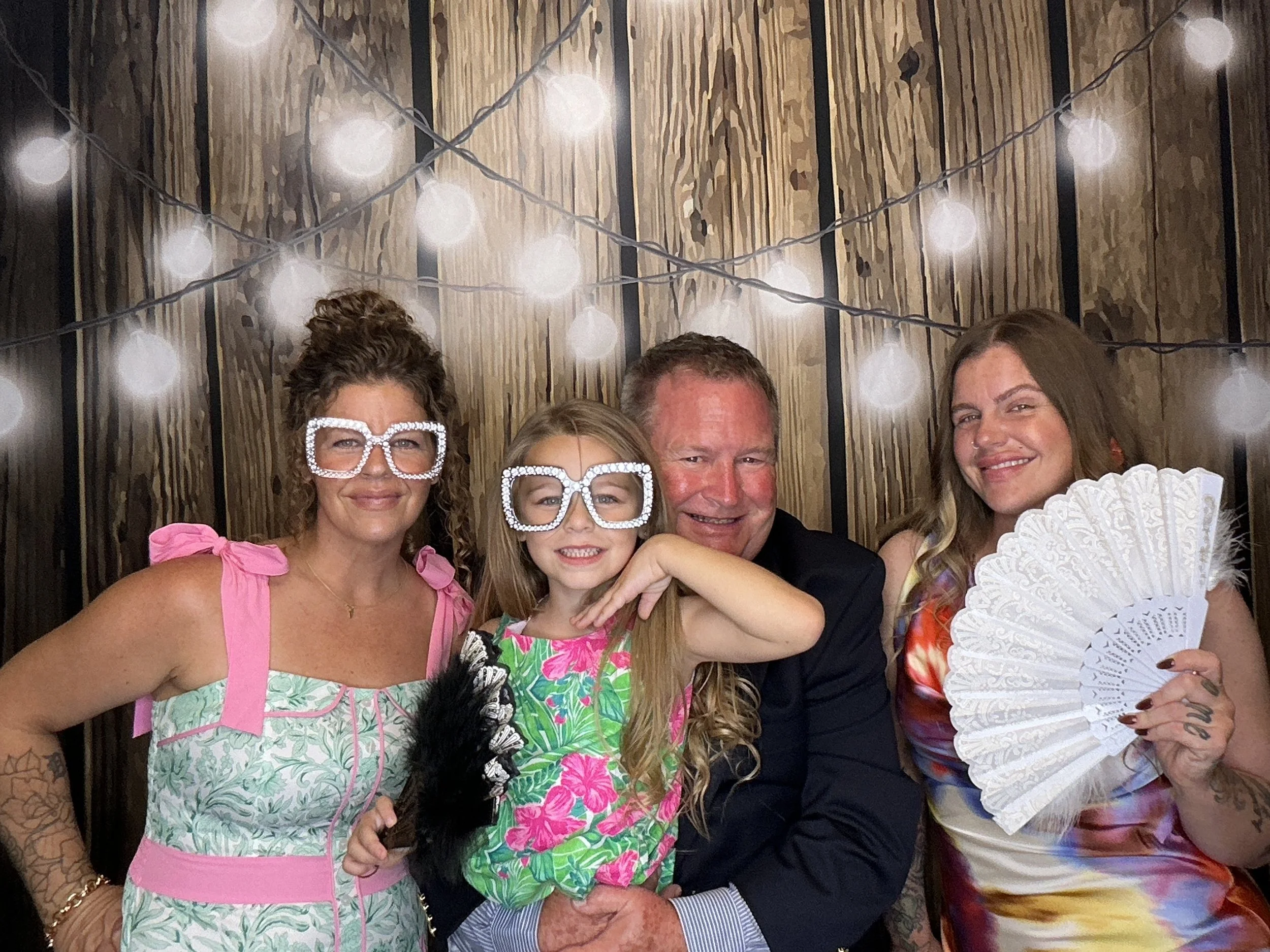 Family posing together with fun Photo Booth props and novelty glasses in front of a wood backdrop with string lights in Orlando, Florida.
