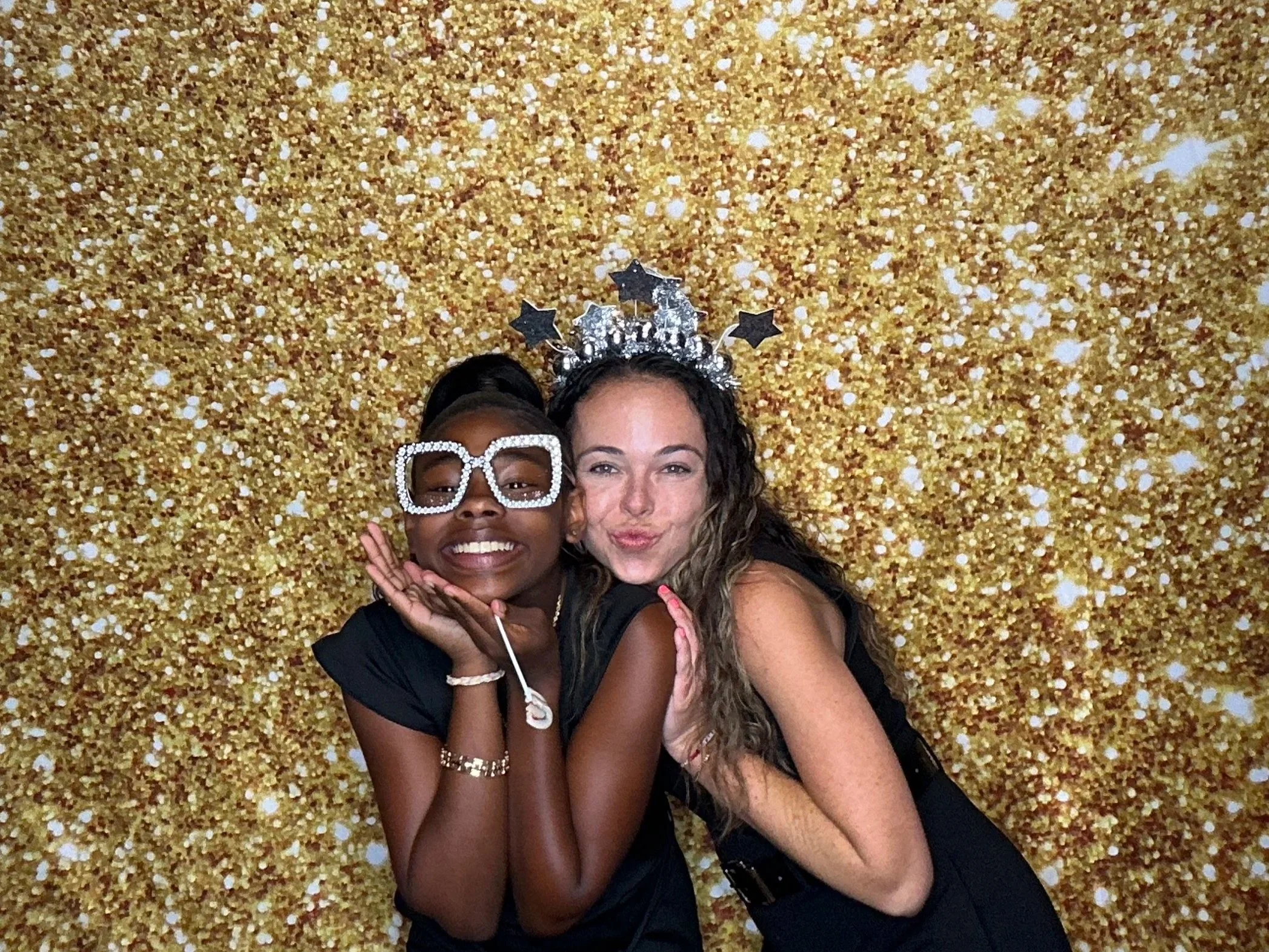 Guests enjoy a Pop & Pose Events Photo Booth rental in Sanford, Fl, posing infant of a gold shimmer backdrop during a celebration.