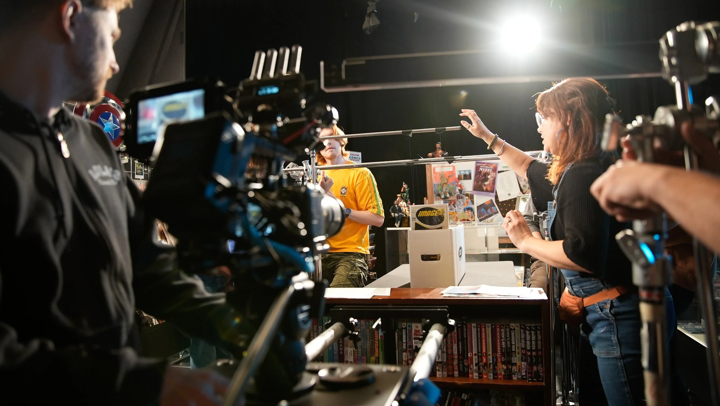 People filming a scene inside a comic store, with shelves of comics and posters in the background.