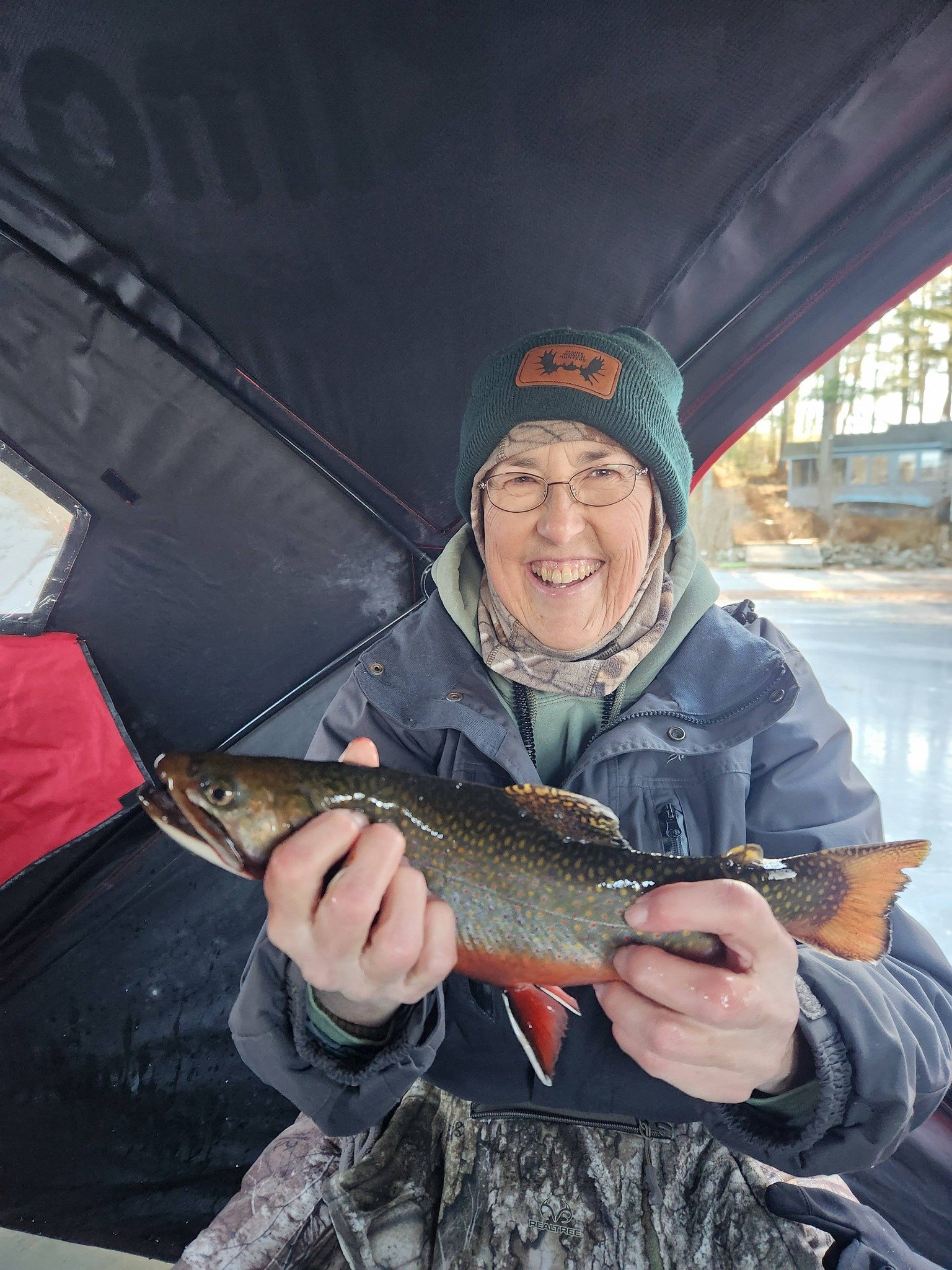 Woman sitting in a pop-up ice shack smiling and holding a brook trout.