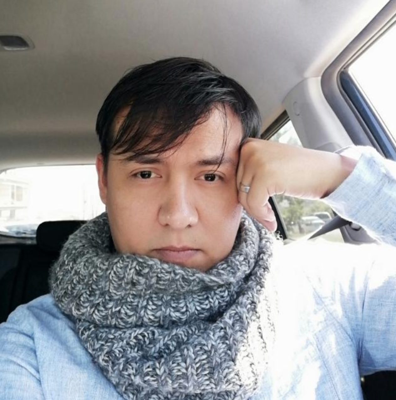 Persona usando un suéter azul claro con bufanda gris dentro de un automóvil.