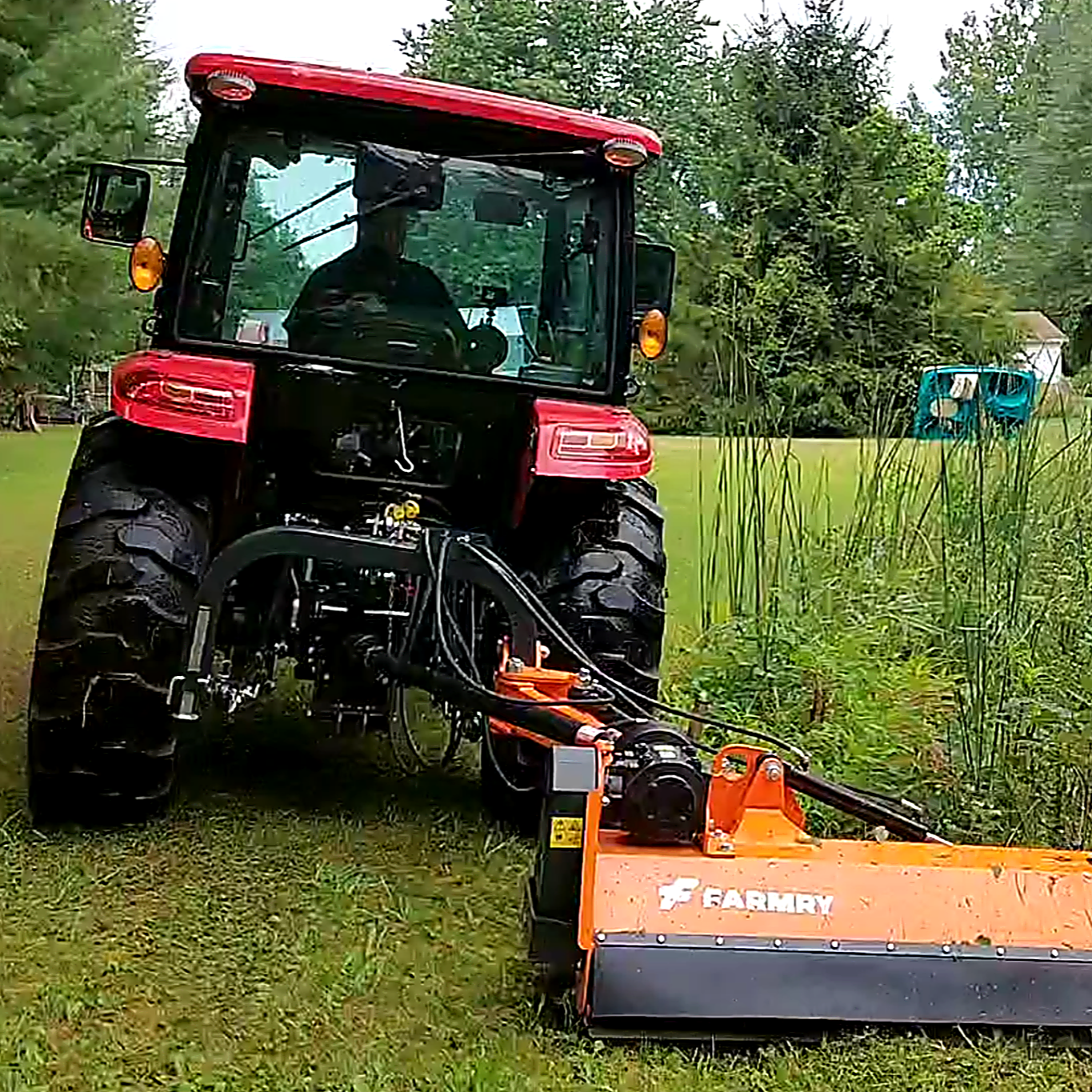 A red tractor with a mowing attachment cutting grass in a lush backyard with trees and a green lawn.