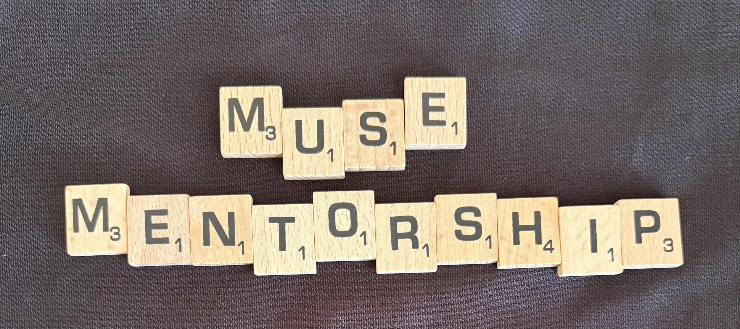 Wooden Scrabble tiles spelling out 'MUSE' and 'MENTORSHIP' on a dark surface.