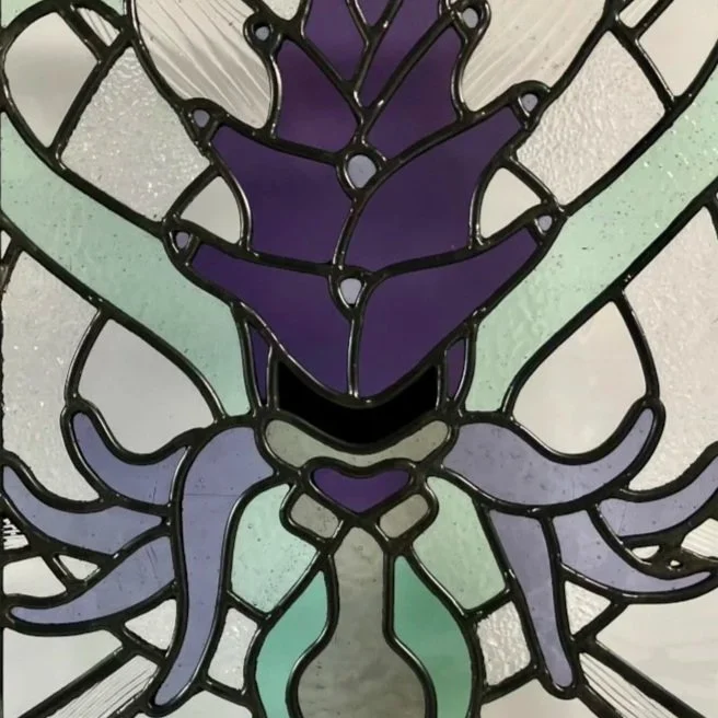Colorful stained glass window depicting a whimsical flower of the Lobster Bush plant with violet tendrils and lilac purple petals, holding two green snakes captivated.