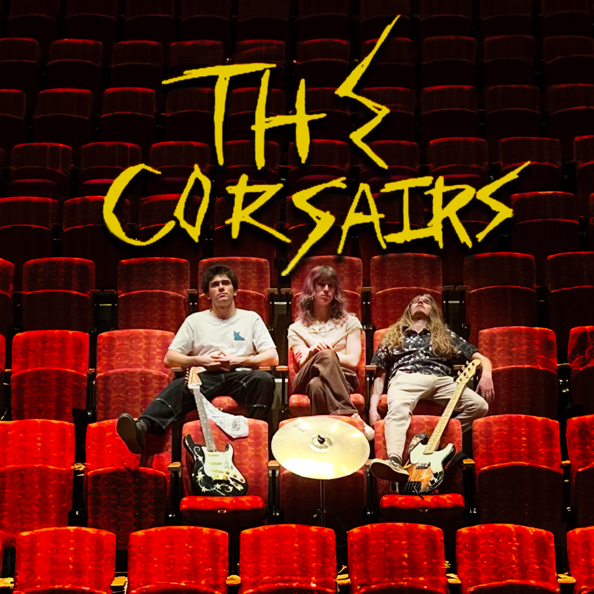Three band members sitting in empty red theater seats with musical instruments, behind a sign that says "This Cursairs."