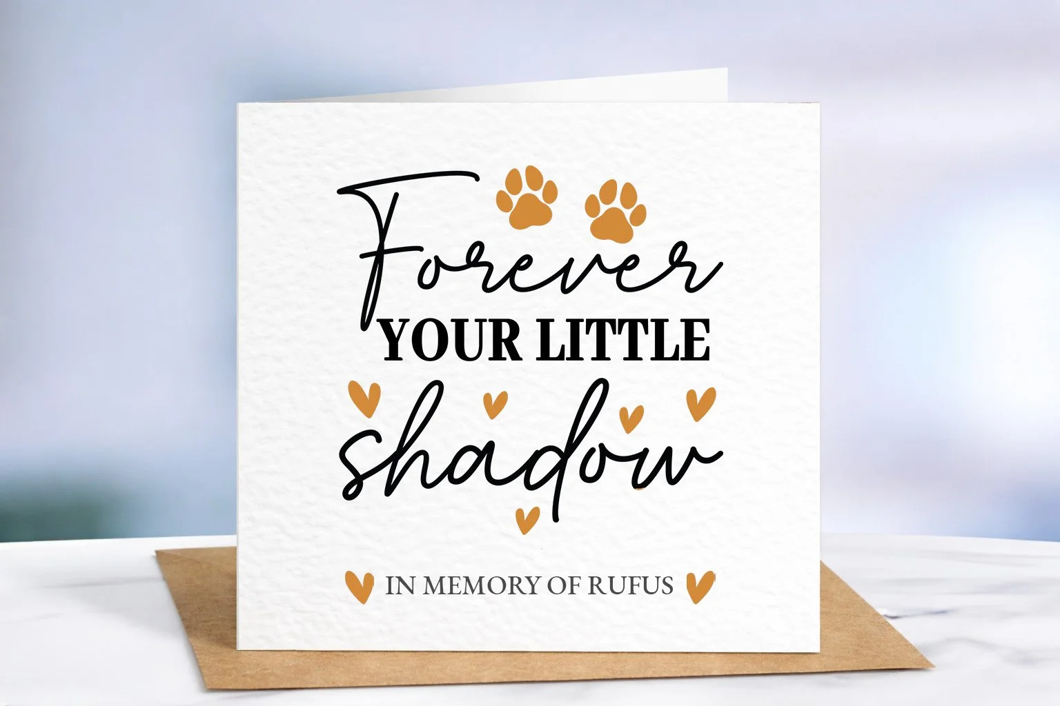Personalised pet memorial card with “Forever Your Little Shadow” text, orange paw prints and hearts, displayed on textured cardstock with kraft envelope