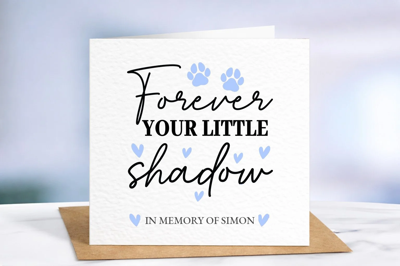 Dog memorial card with blue paw prints and hearts, personalised with name Simon, displayed on premium textured cardstock