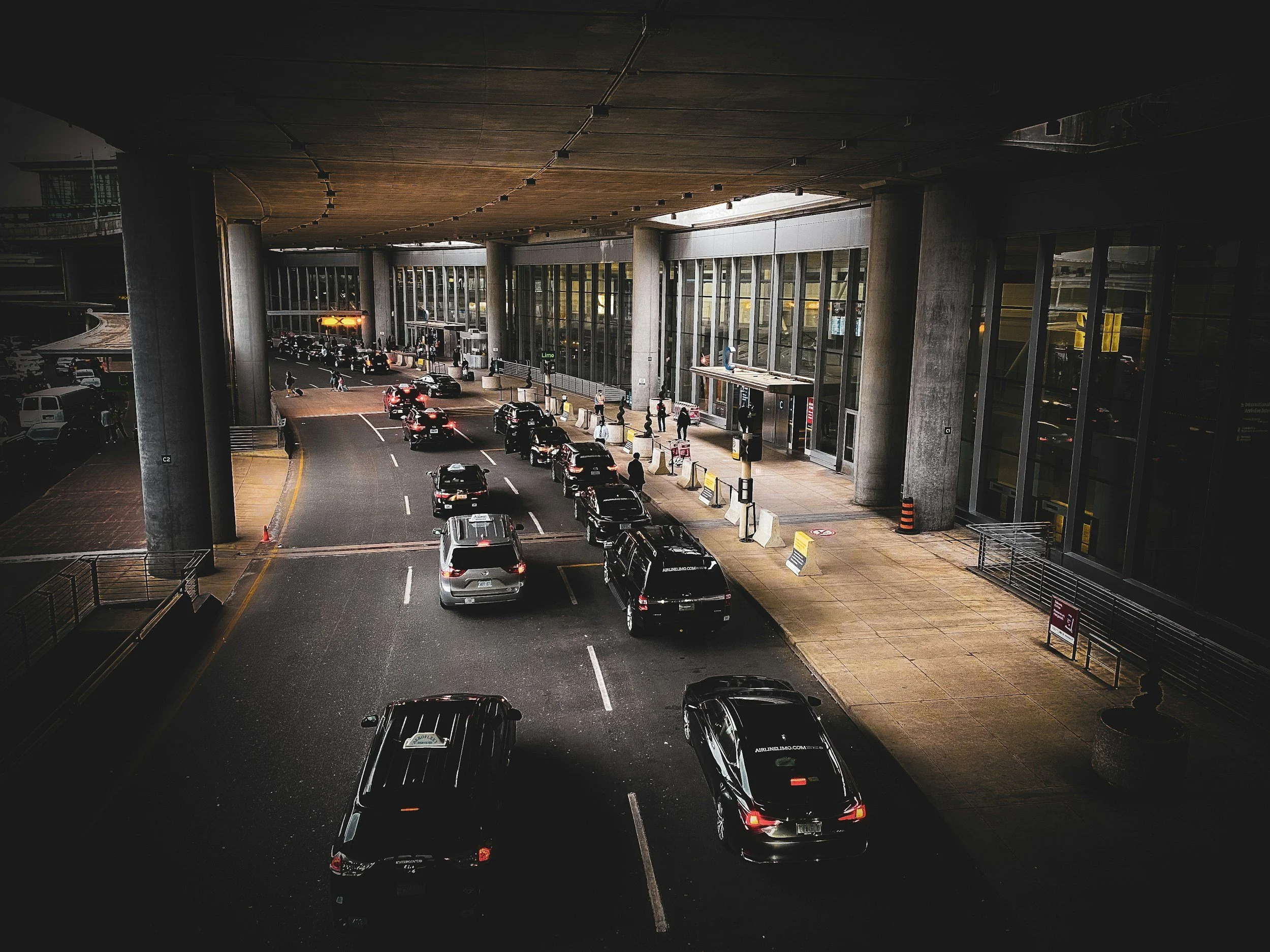 Vehicles parked and being loaded at a modern airport terminal entrance during evening.