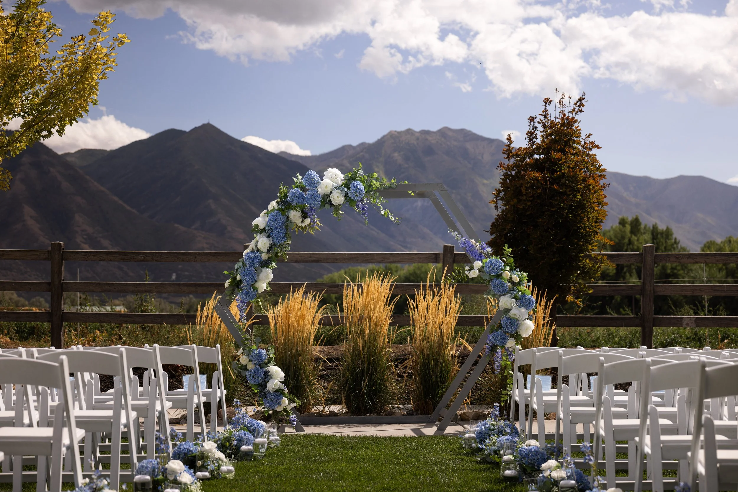 Outdoor wedding venue with white chairs, a floral hexagon arch, and mountain backdrop