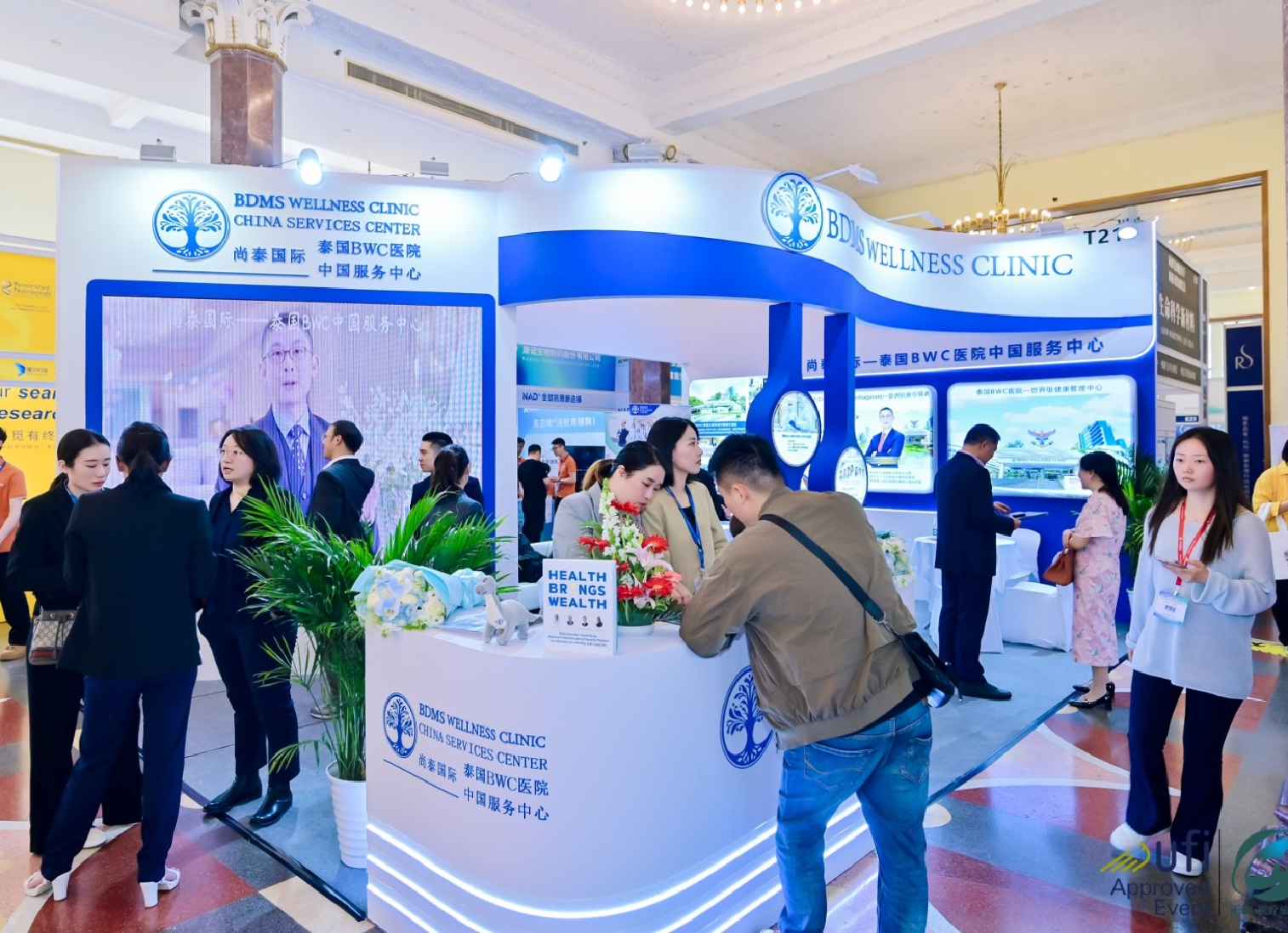 Exhibition booth for BDMS Wellness Clinic at a conference, with several people interacting and promotional displays about healthcare and wellness.
