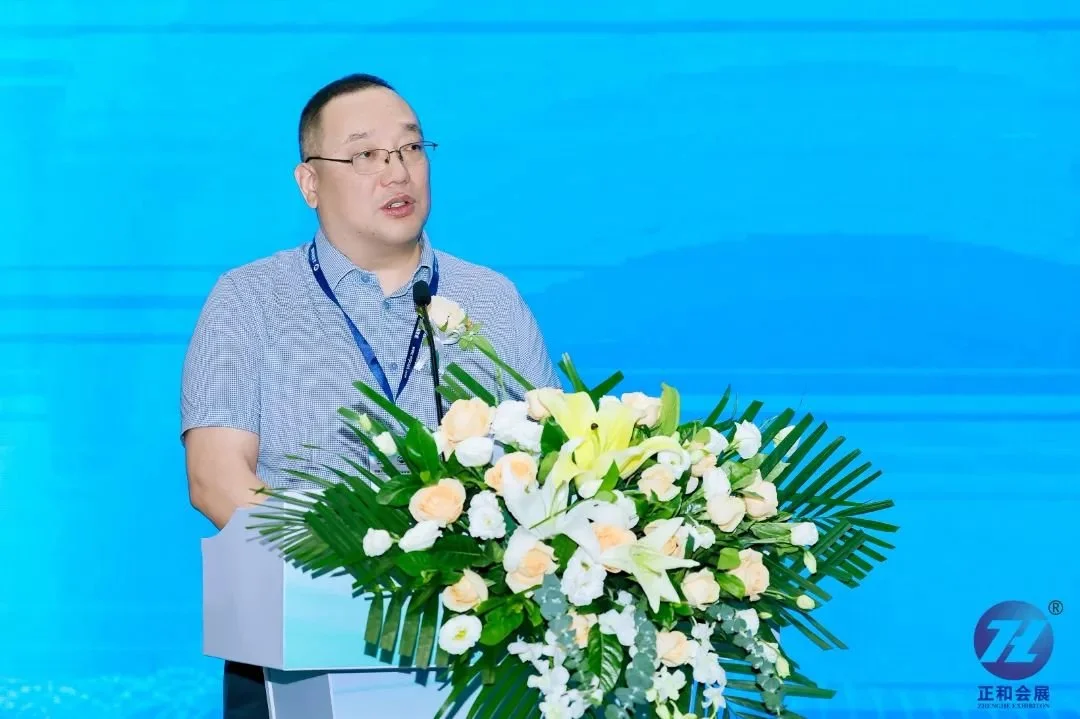 A man speaking at a podium decorated with a large floral arrangement of white and peach flowers, with a blue background.